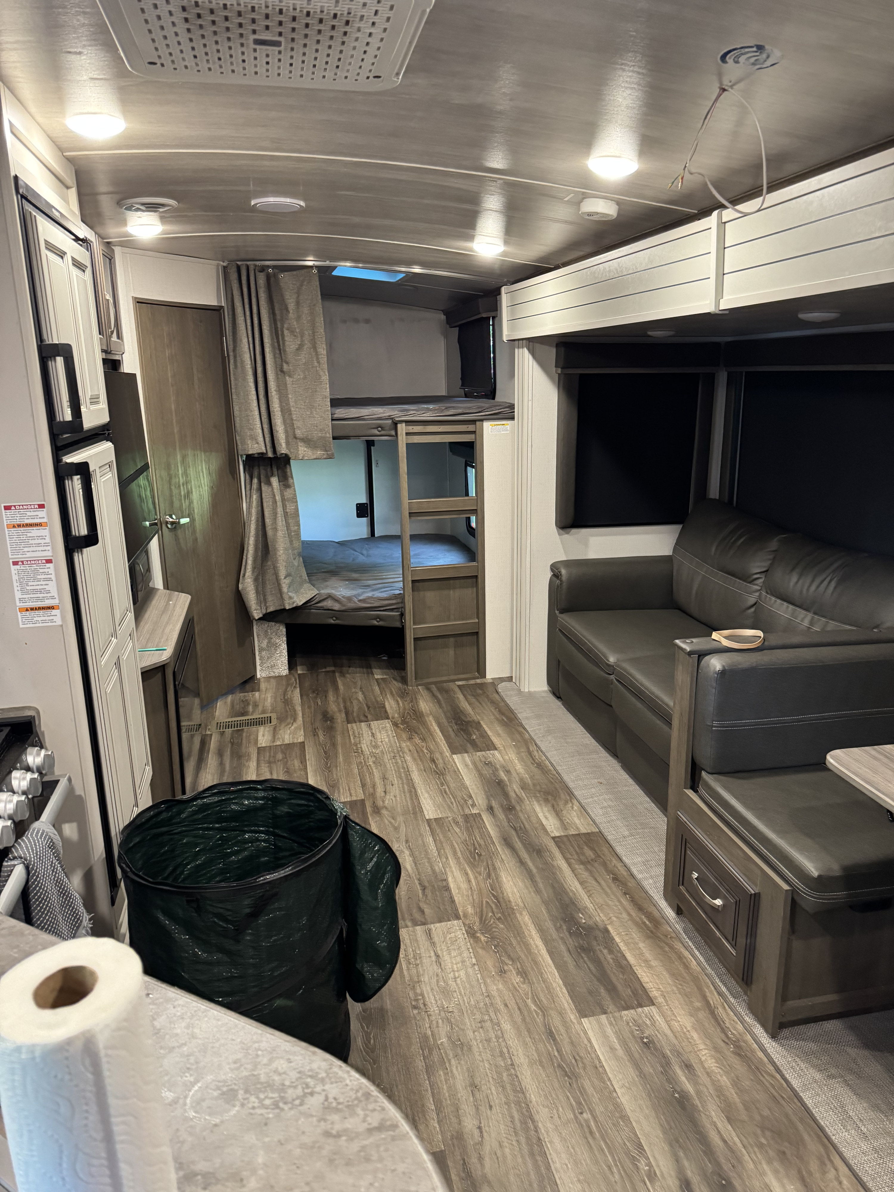 RV rental interior: living area with sofa, bunk beds, and kitchen. Note the wire hanging from the ceiling in this camper.. Keystone RV Cougar 2022