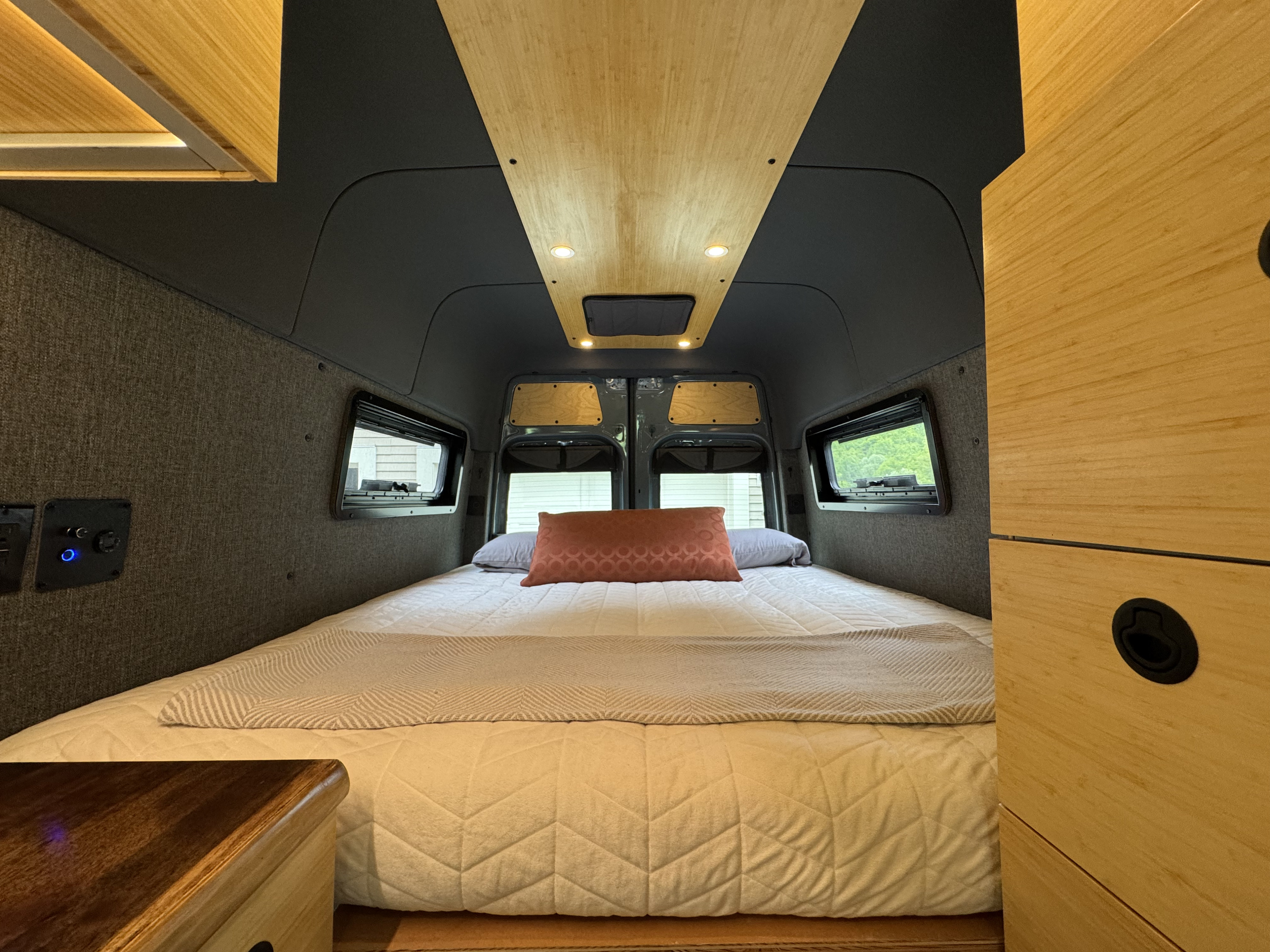 Relaxing RV rental interior showcasing a large bed, stylish wood ceiling & cabinetry, ambient lighting, and side windows.. Mercedes-Benz Sprinter 2021