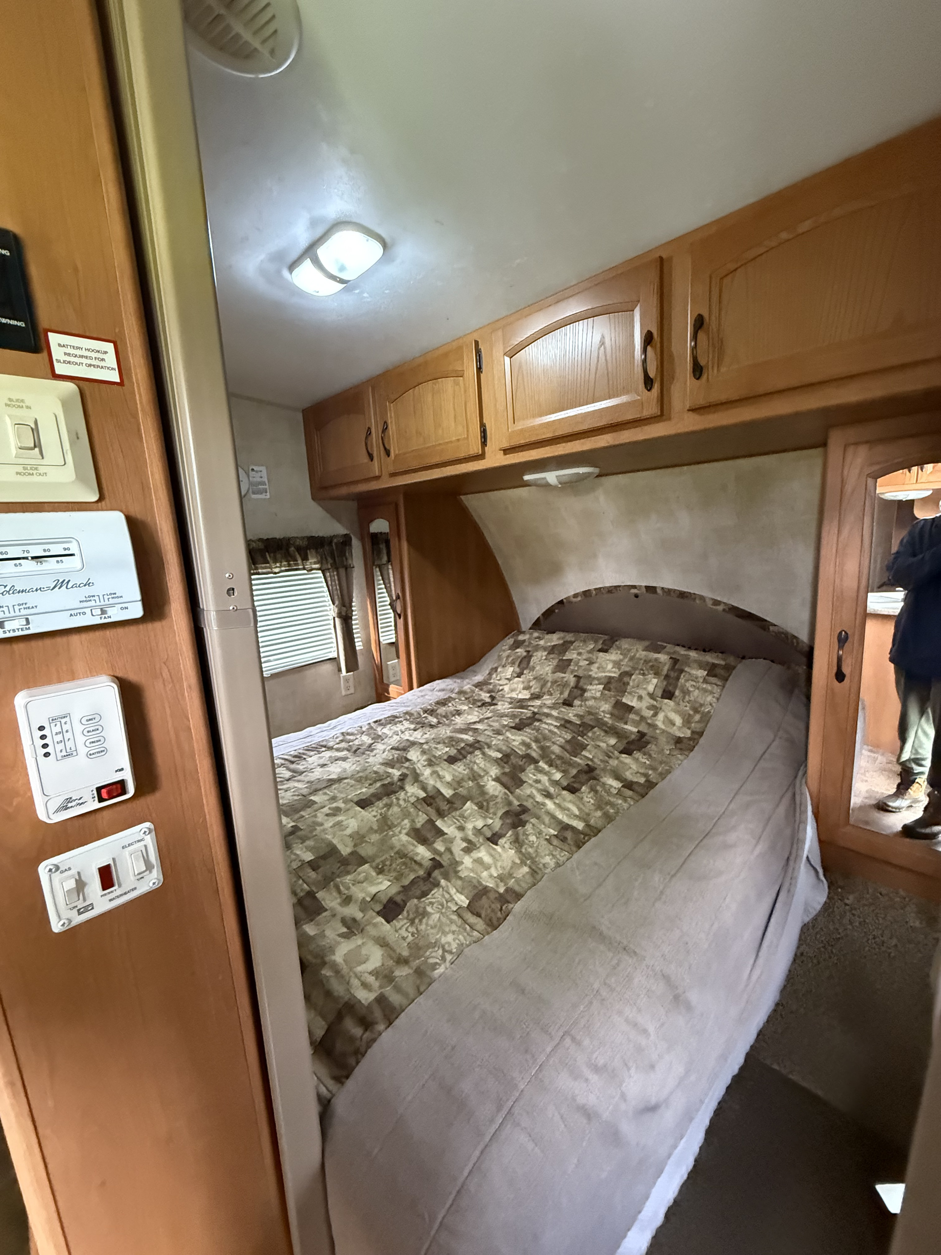RV rental bedroom with compact living space, featuring a bed, overhead cabinets, and essential control panels.. Keystone RV Hornet 2011