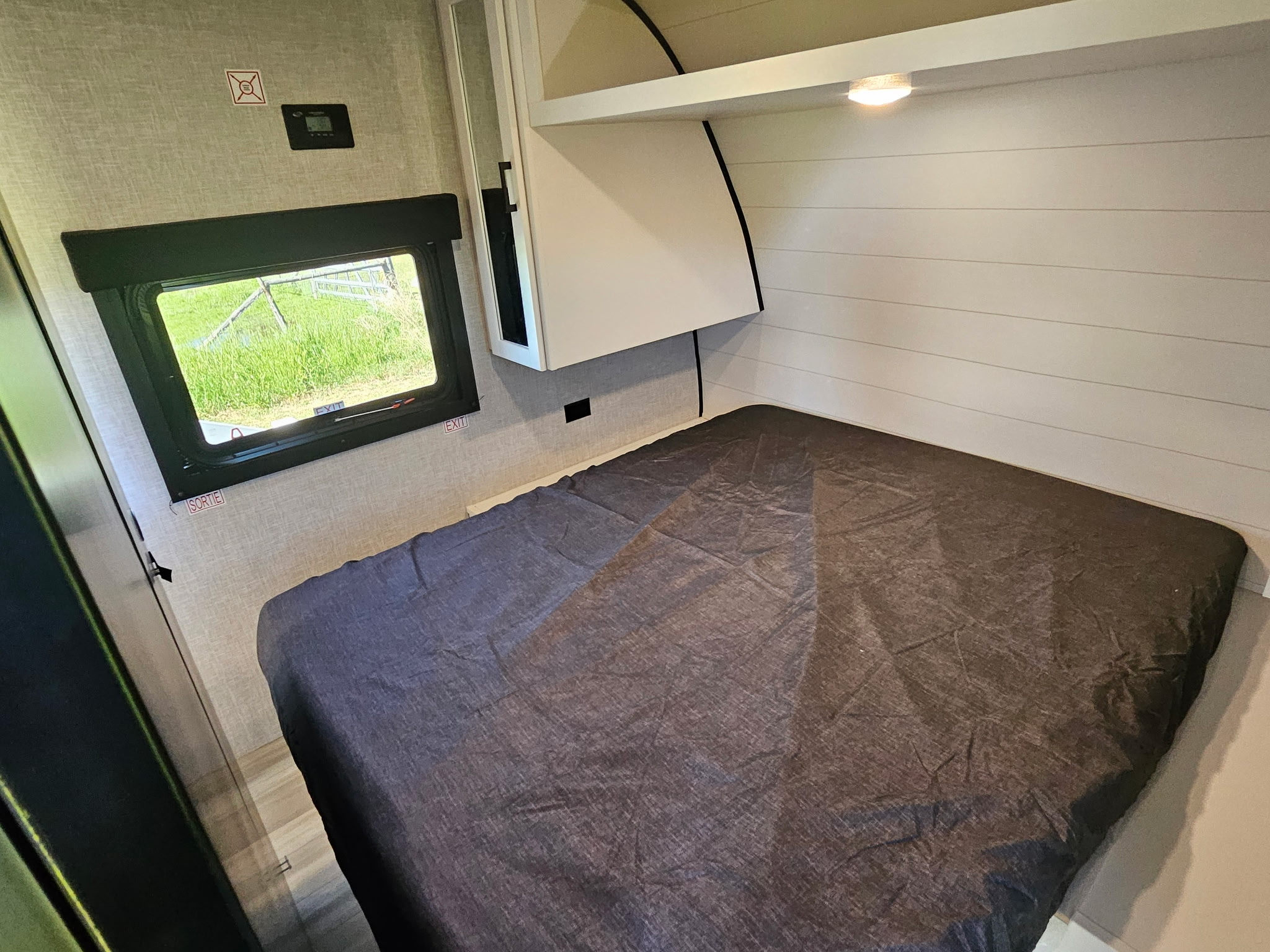 Cozy RV rental interior: A compact bedroom with a bed, window looking out to green grass, and built-in storage.. Highland Ridge Open Range 26BHS 2025