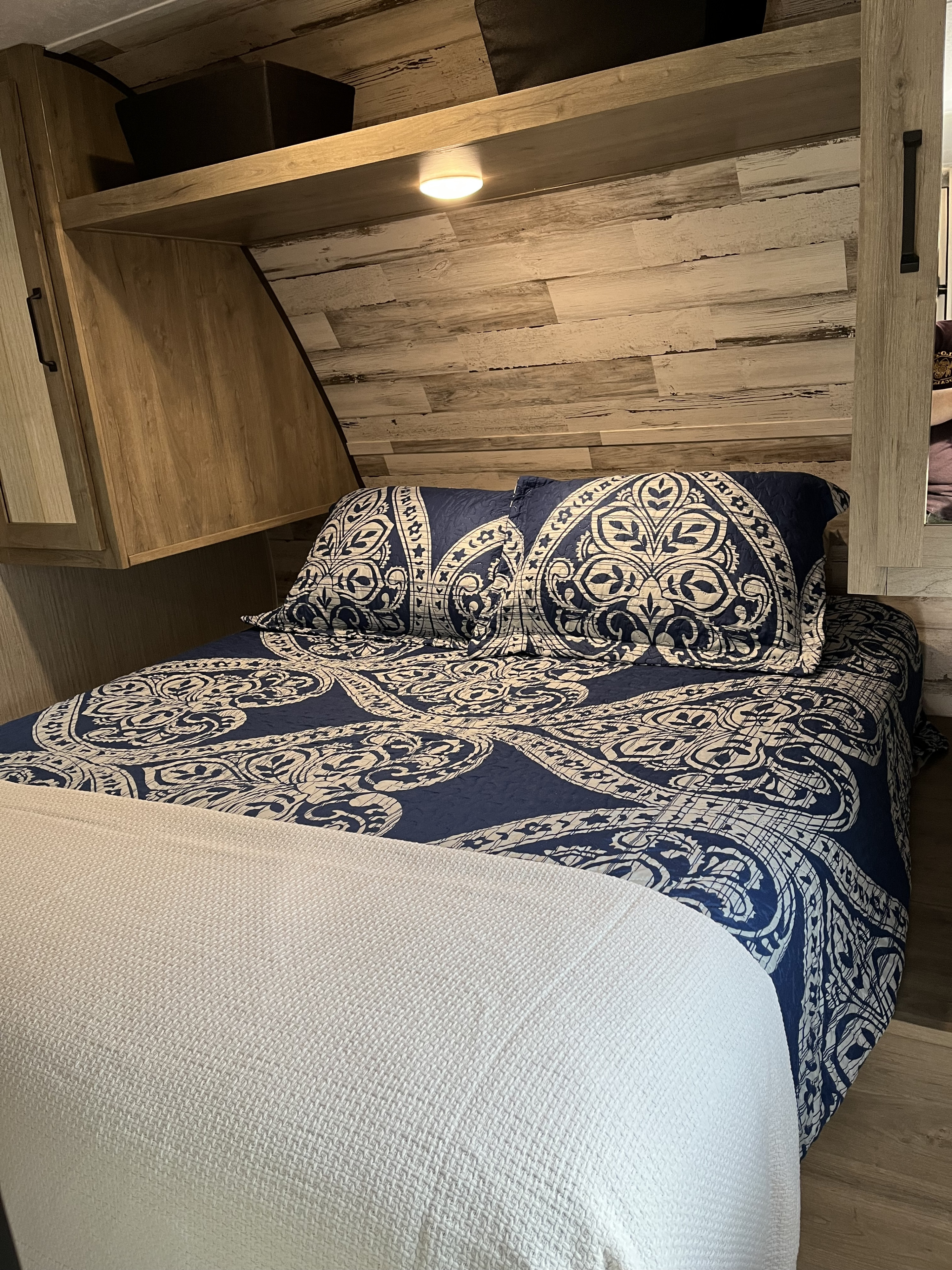 Inviting rv rental bedroom showing a bed with blue patterned covers & overhead light/storage.. Forest River Palomino Puma XLE Lite 2021