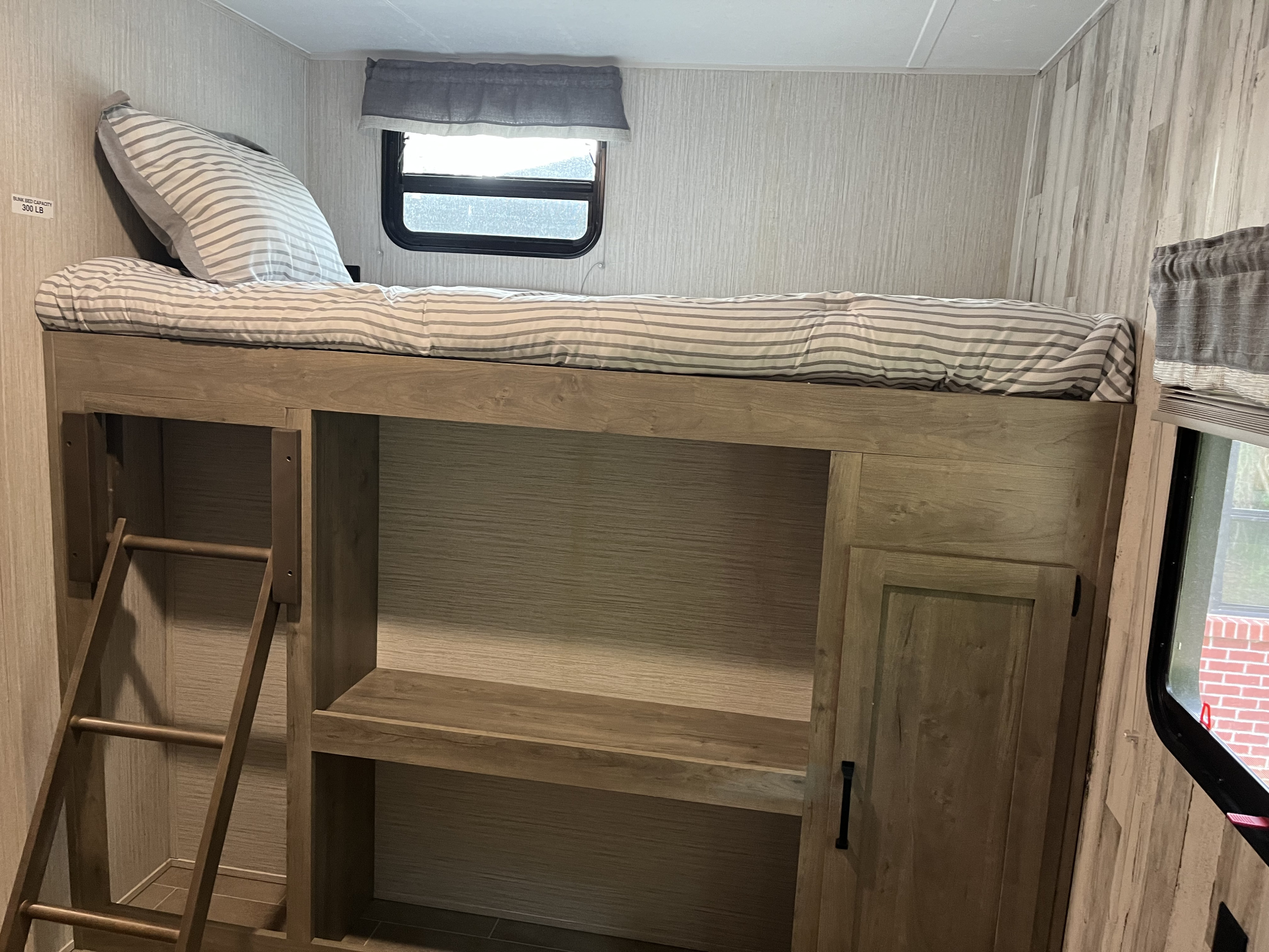 Interior of an RV rental: a comfortable bunk bed with striped bedding, ladder access, window, and built-in storage.. Forest River Palomino Puma XLE Lite 2021