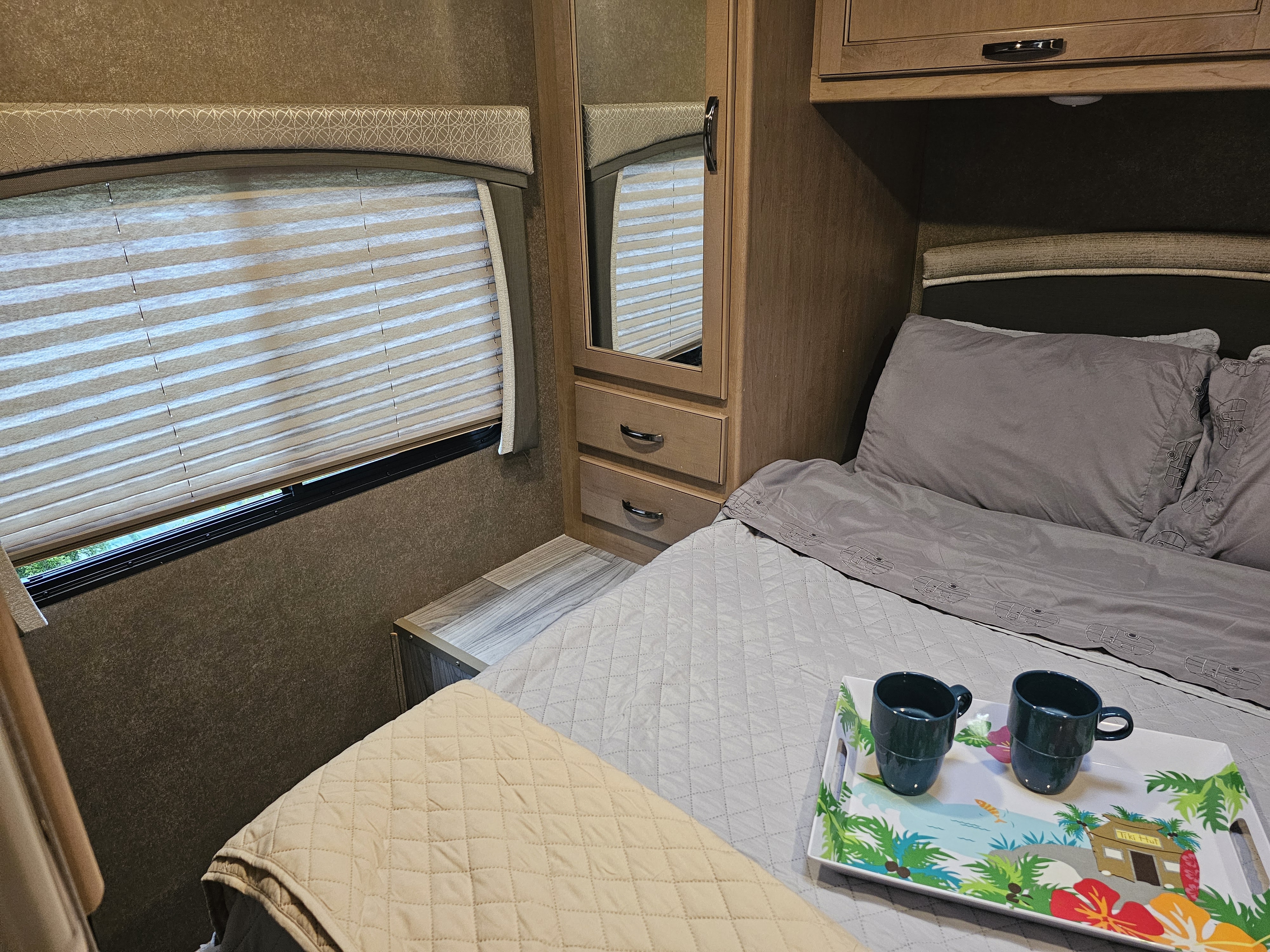 Cozy RV rental bedroom with a comfortable bed, window blinds, built-in storage, and a tray with two mugs. Perfect for travel!. Thor Four Winds 2021