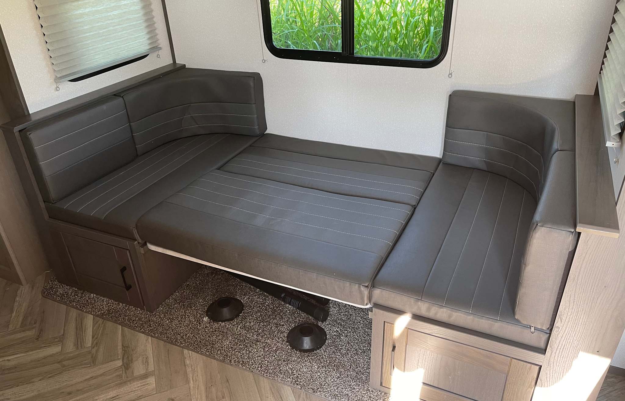 This RV rental features a comfortable gray convertible dinette bed with sleek cushions, stylish wood-look cabinetry, and a window view.. Cruiser RV Shadow Cruiser 2019
