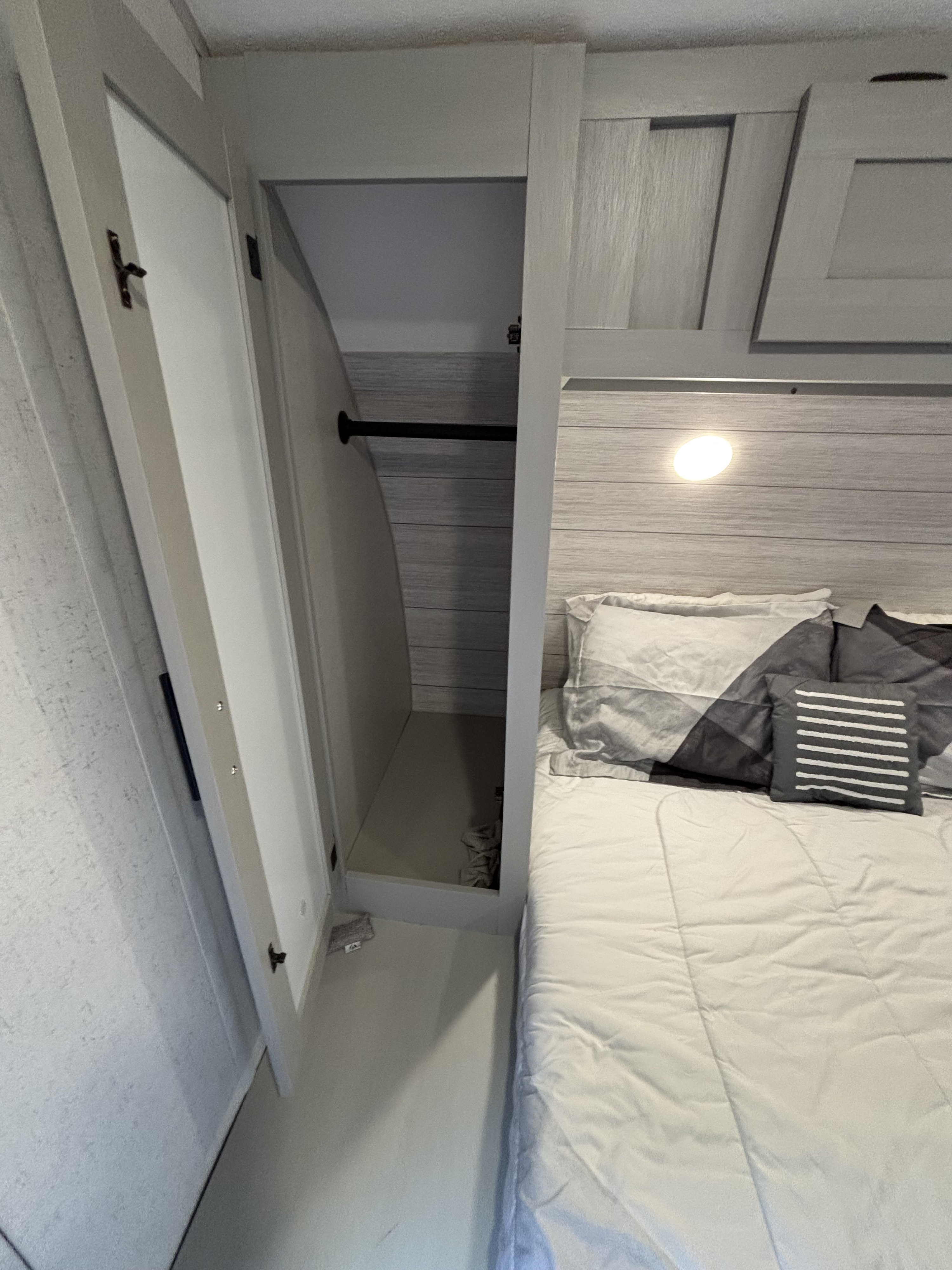 Cozy RV rental bedroom showing a comfortable bed and an open wardrobe with a hanging bar. Compact and functional.. Forest River Salem FSX Platinum Toy Hauler 2022