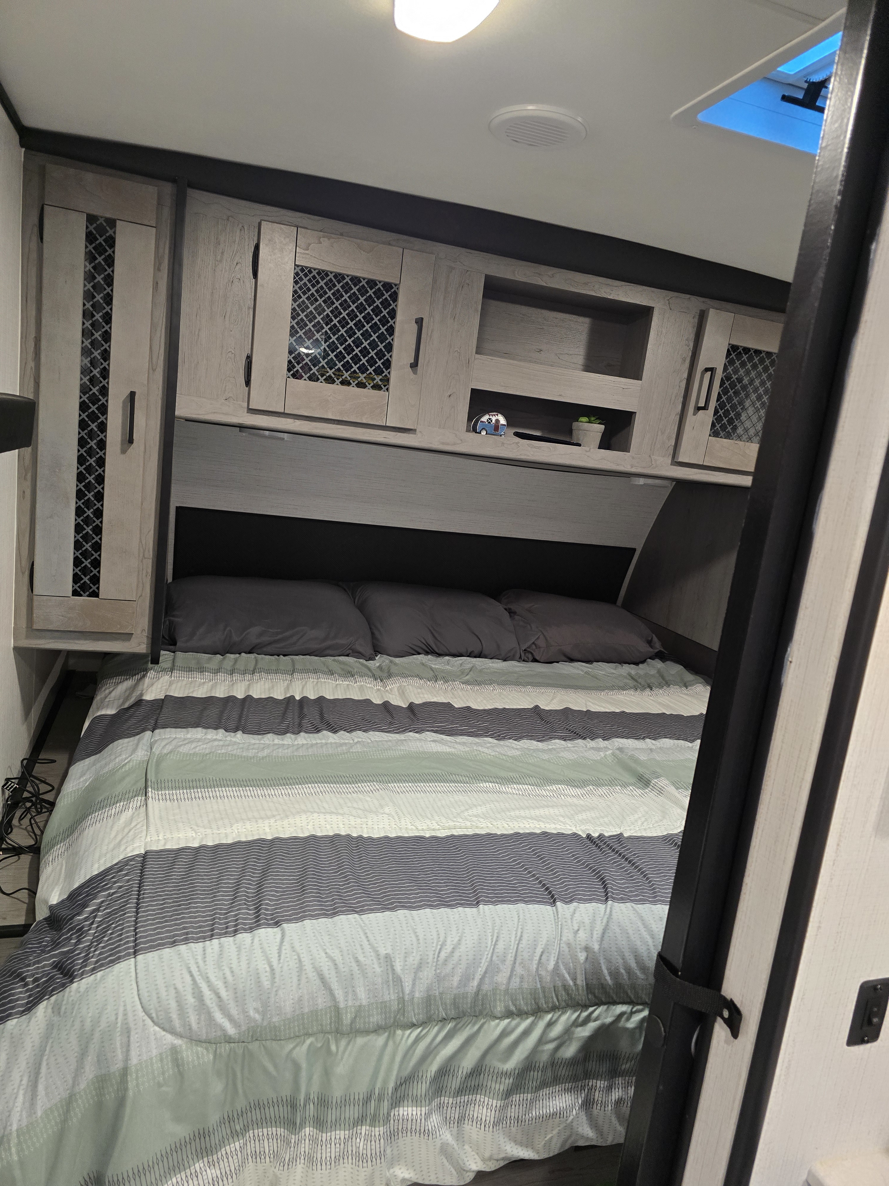 Cozy RV rental bedroom featuring a comfortable striped bed, overhead cabinets for storage, and a bright skylight.. Heartland RVs Mallard 2022