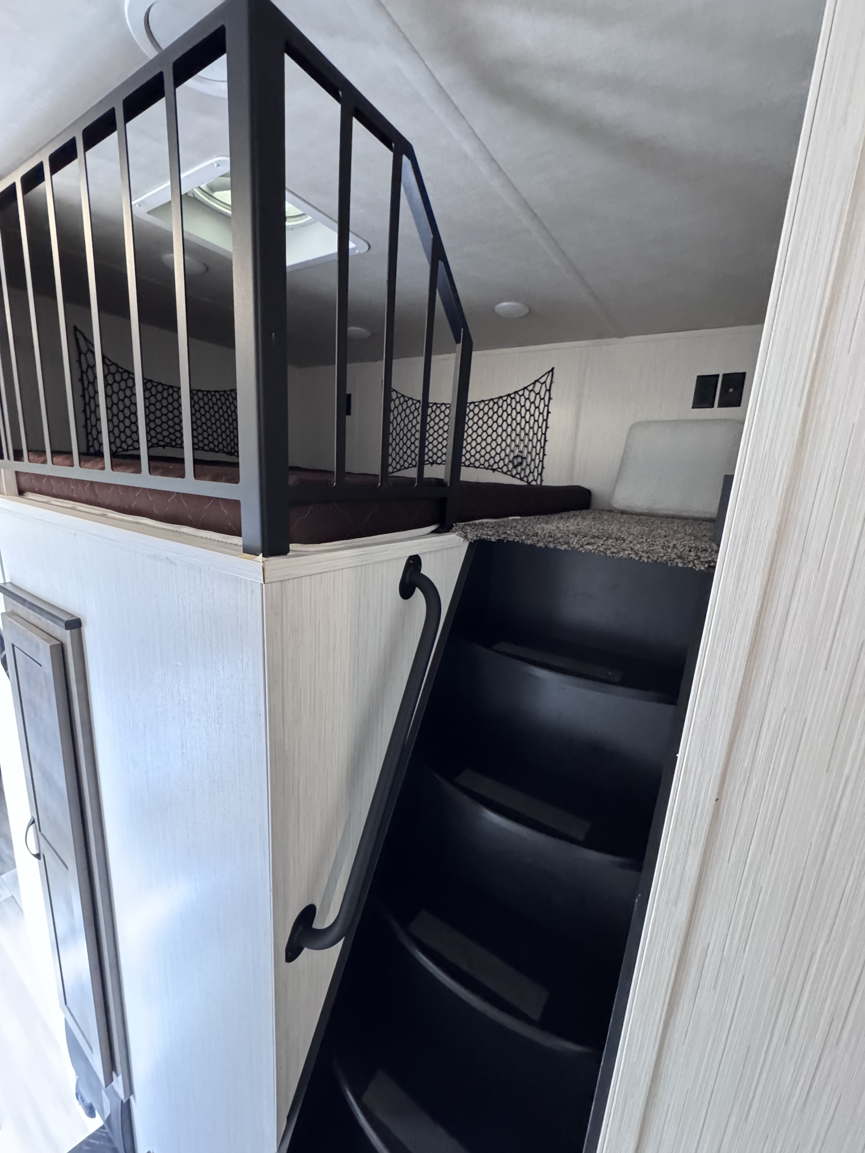 RV rental interior view of a loft with two bunk beds, black safety rails and netting, accessed by black, integrated stairs.. Forest River Cedar Creek 2022