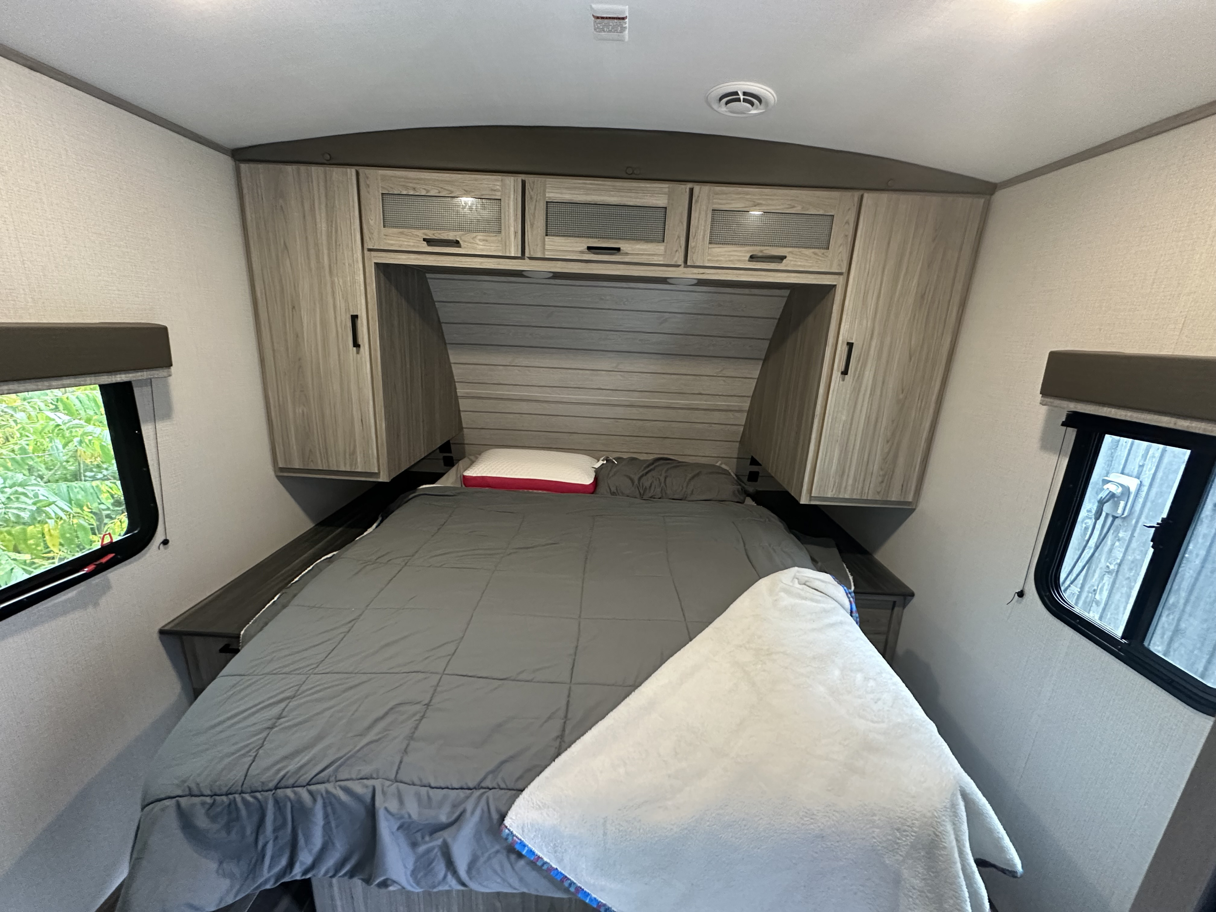 A cozy RV rental bedroom features a comfy bed, overhead cabinets, and windows providing natural light and views.. Keystone RV Passport GT 2022