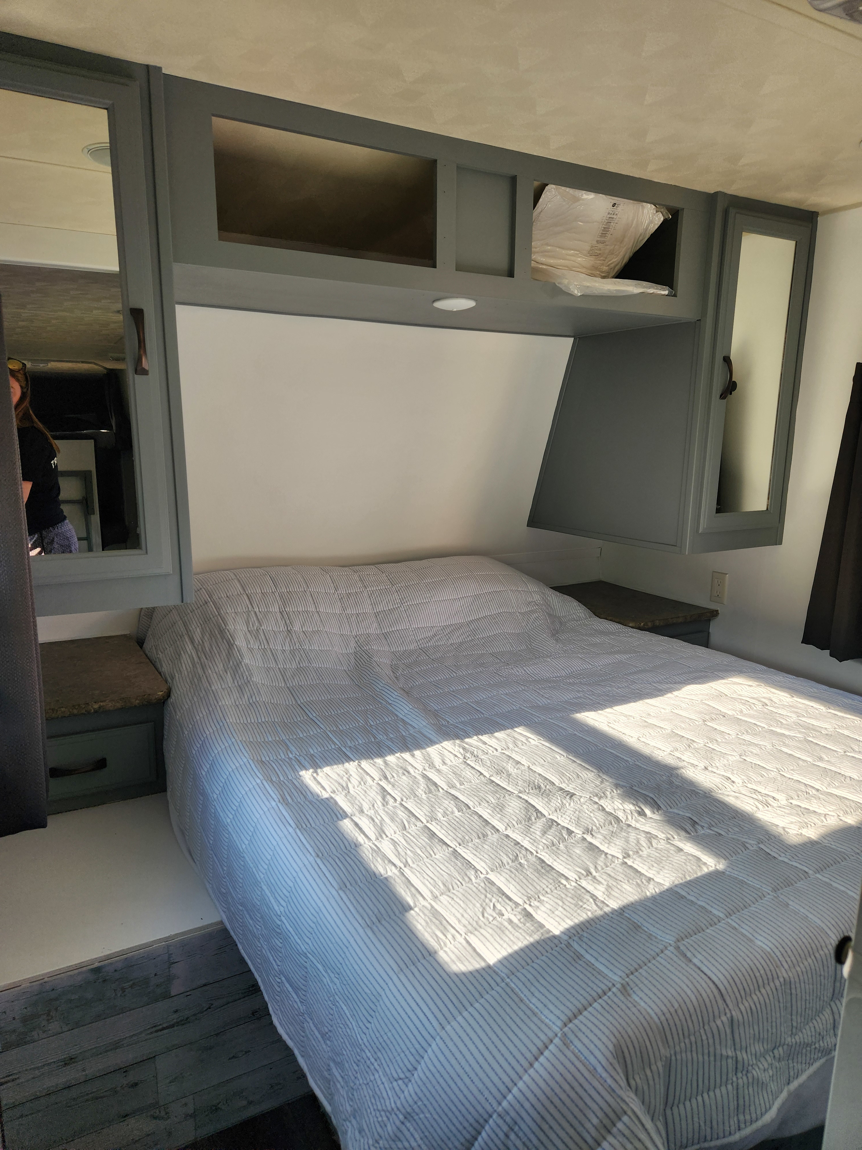 Cozy RV rental bedroom featuring a striped bed, grey cabinets, and built-in nightstands. Sunlight streams across.. Forest River Palomino Puma 2013