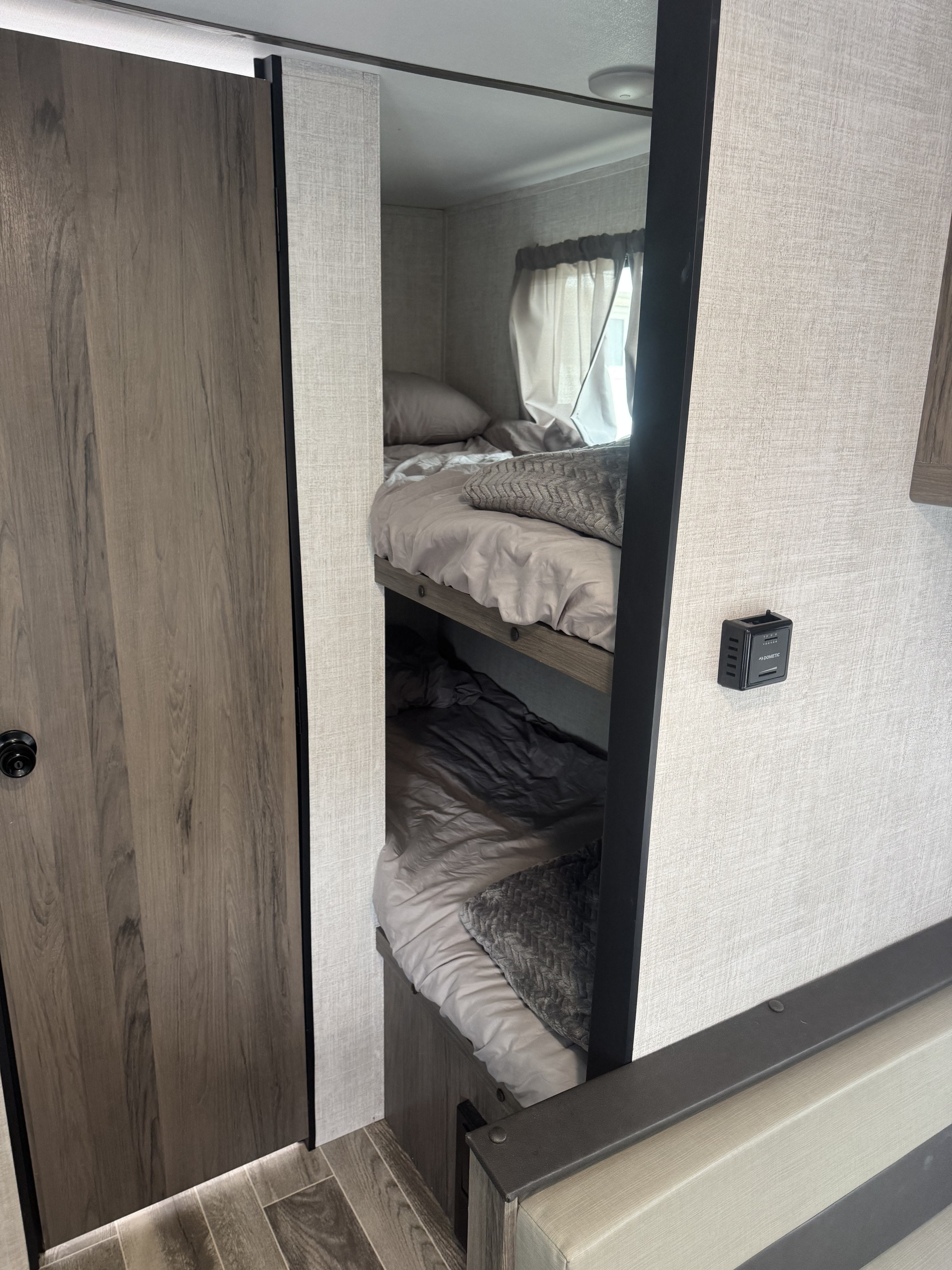 Inside an RV rental: two compact bunk beds with soft bedding, a nearby wooden door, and wall-mounted climate control.. Gulf Stream Ameri-Lite Super Lite 2022
