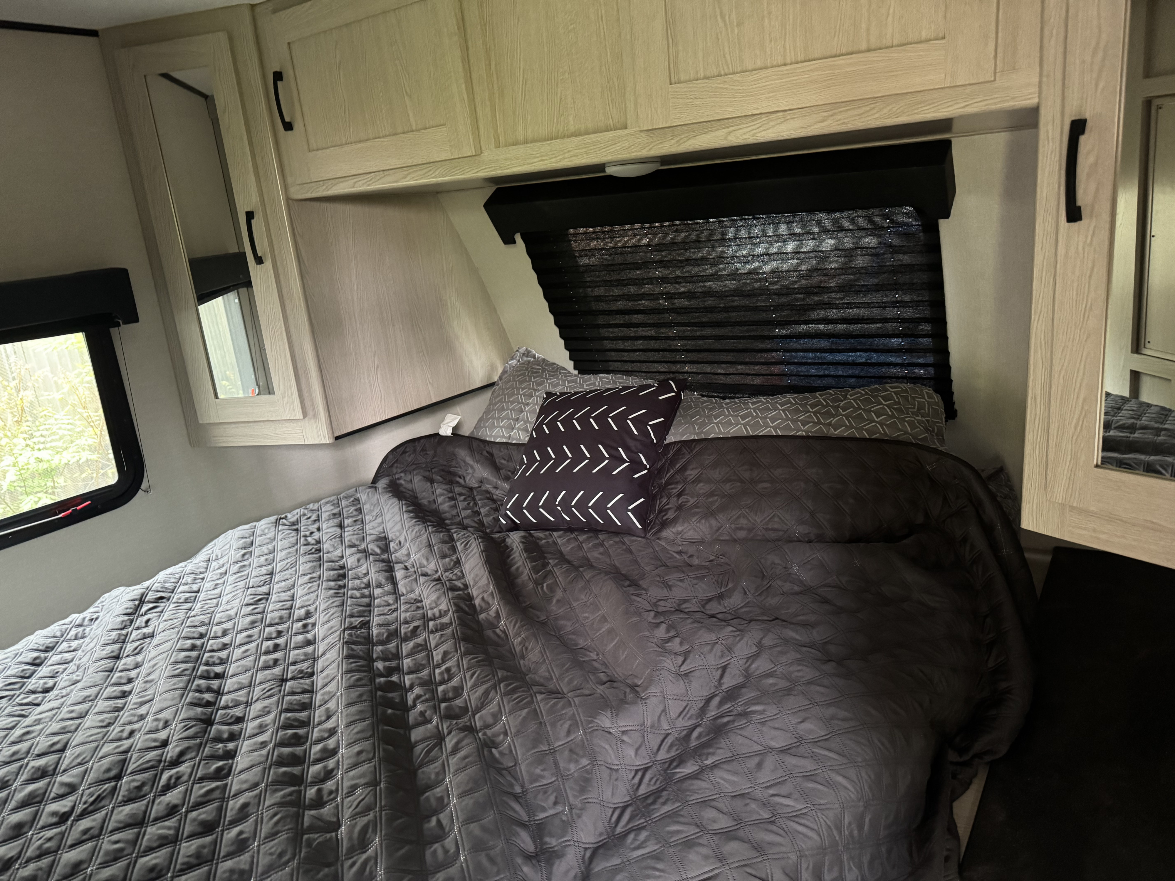 A cozy RV rental bedroom with quilted bedding, patterned pillows, overhead cabinets, and a window. Perfect for your travels.. Coachmen Apex 2022