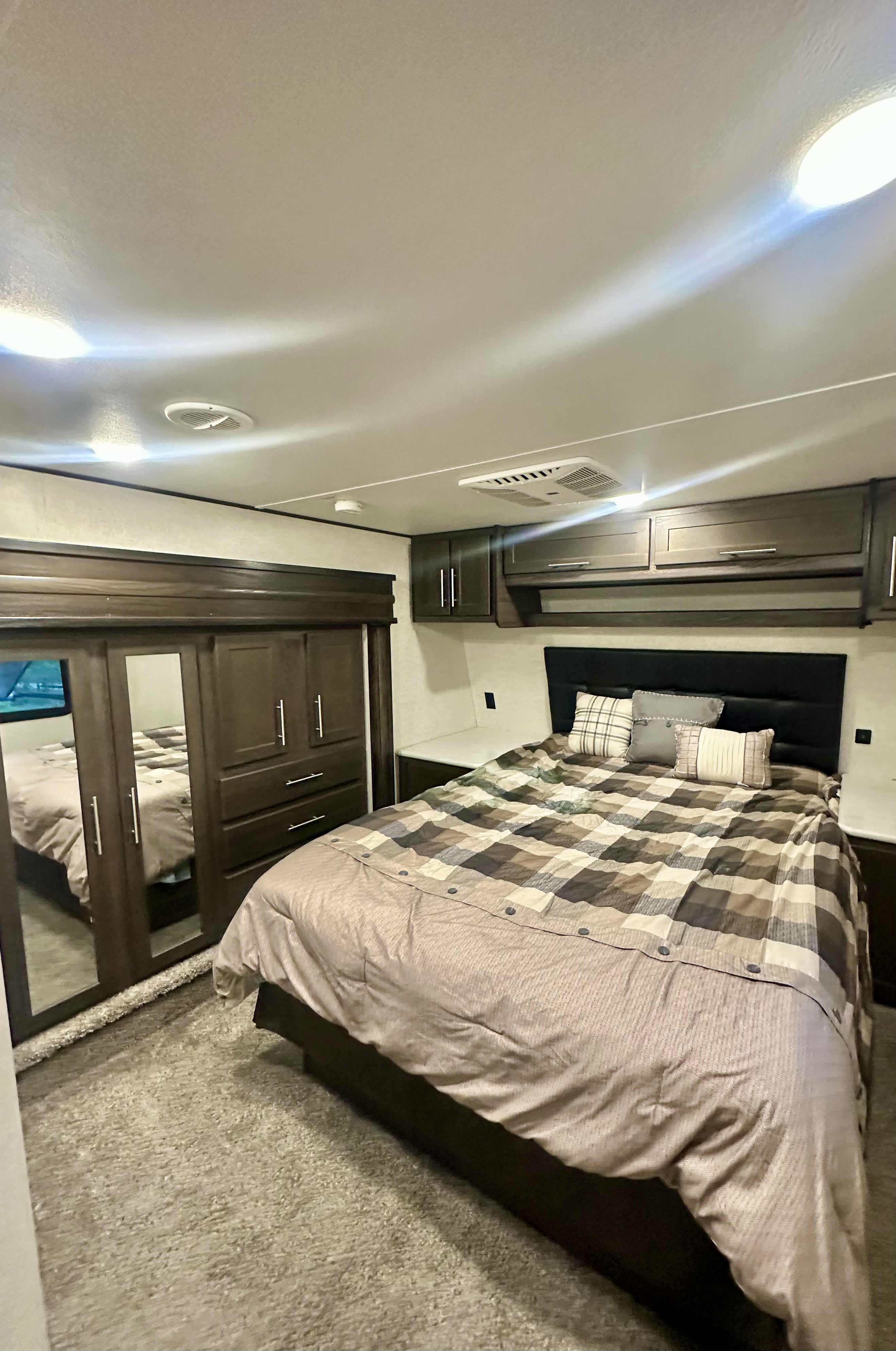 RV rental bedroom with a comfortable bed, plaid comforter, mirrored closet, and dark wood overhead storage cabinets.. Keystone RV Carbon Toy Hauler 2018