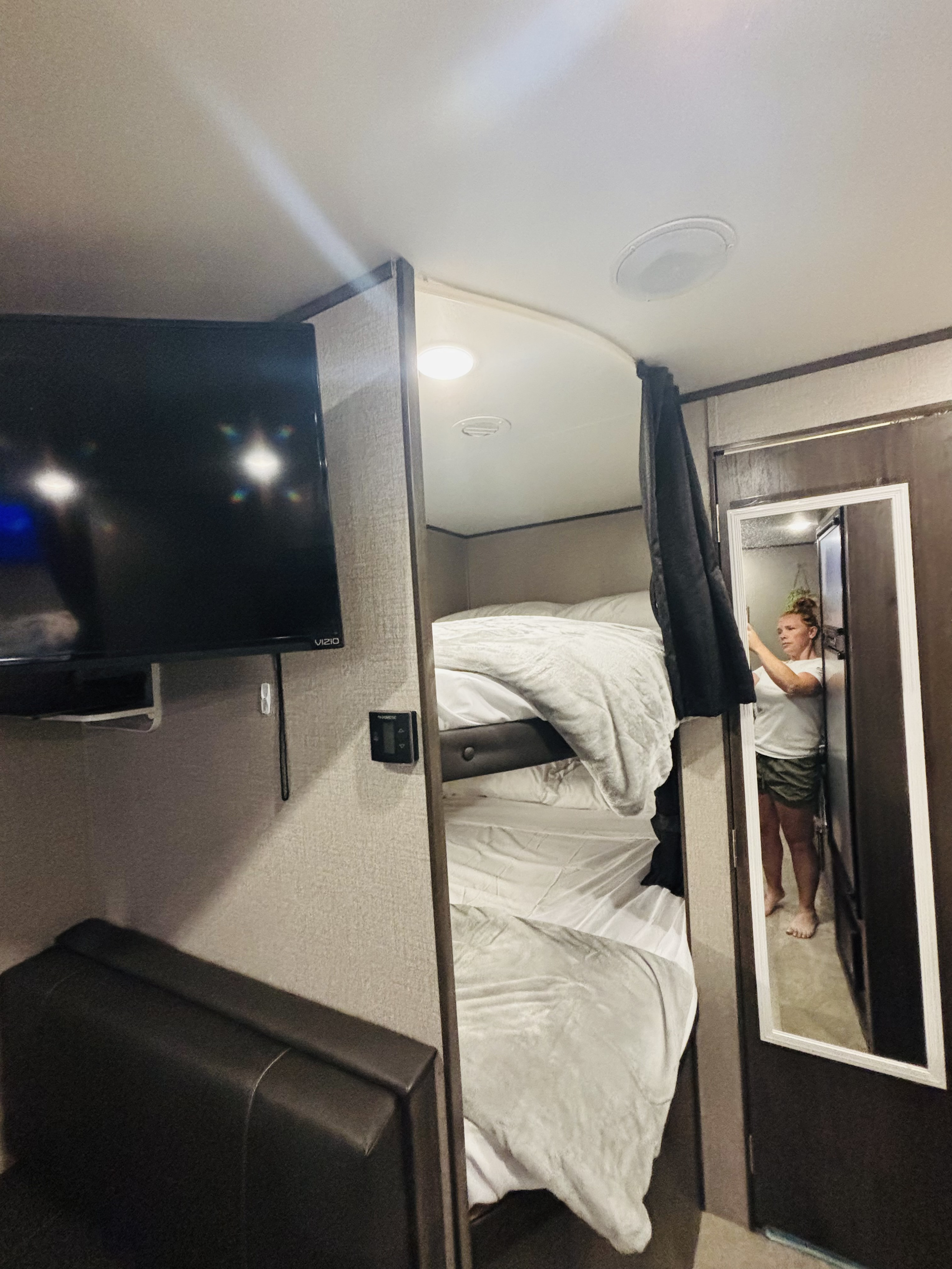 RV rental interior with two neatly made bunk beds, a wall-mounted TV, and a full-length mirror showing a person.. Jayco Jay Flight SLX 2020