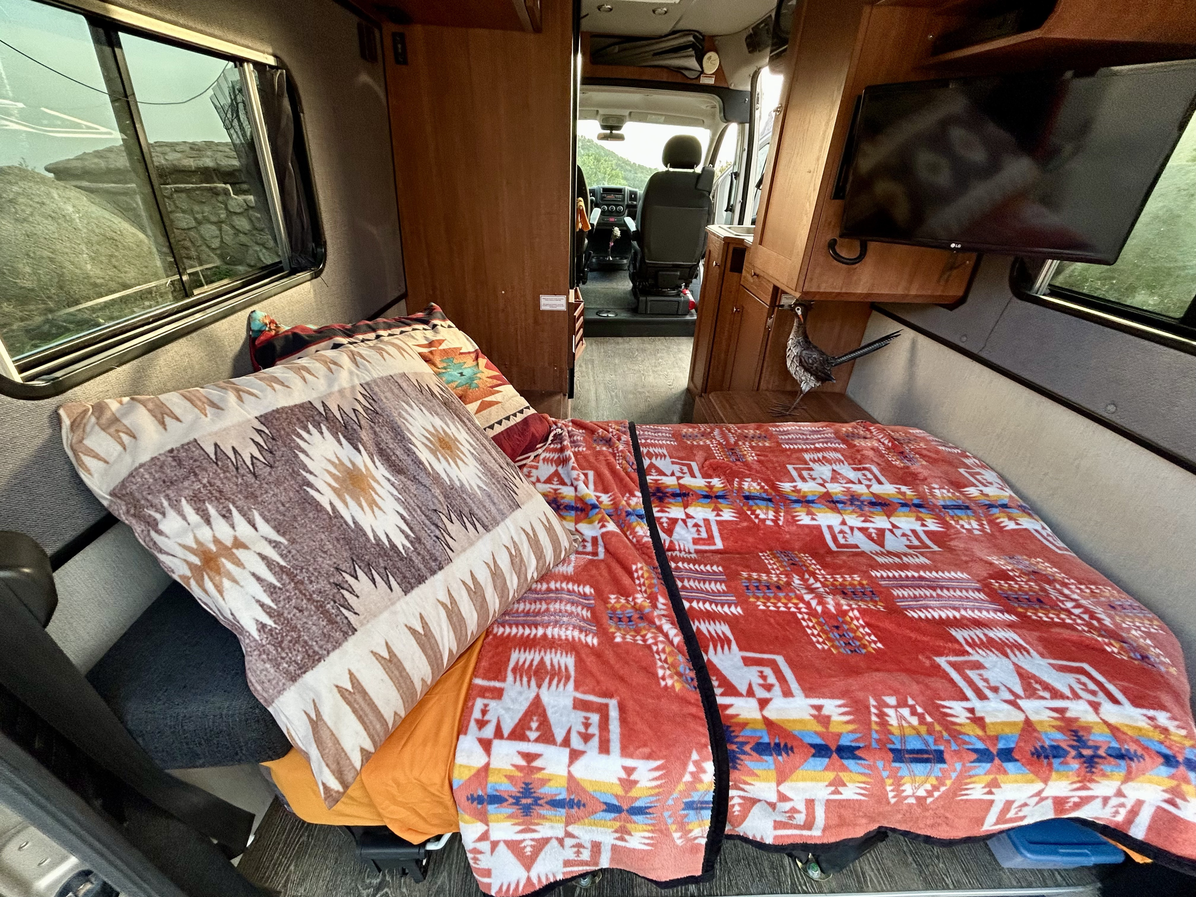 Step into this cozy RV rental interior! Features a bed with vibrant Southwestern blankets, a TV, and scenic window views.. Roadtrek Roadtrek Class B 2019