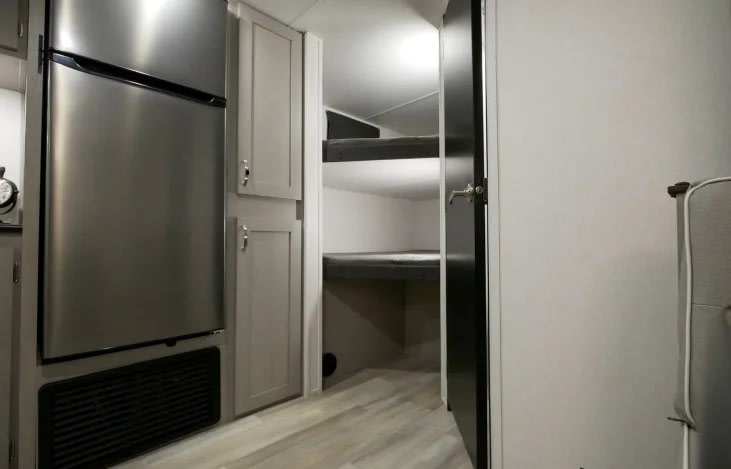 RV rental interior: stainless steel refrigerator, light cabinets, and an open doorway revealing built-in bunk beds.. Primetime RV Tracer 2022