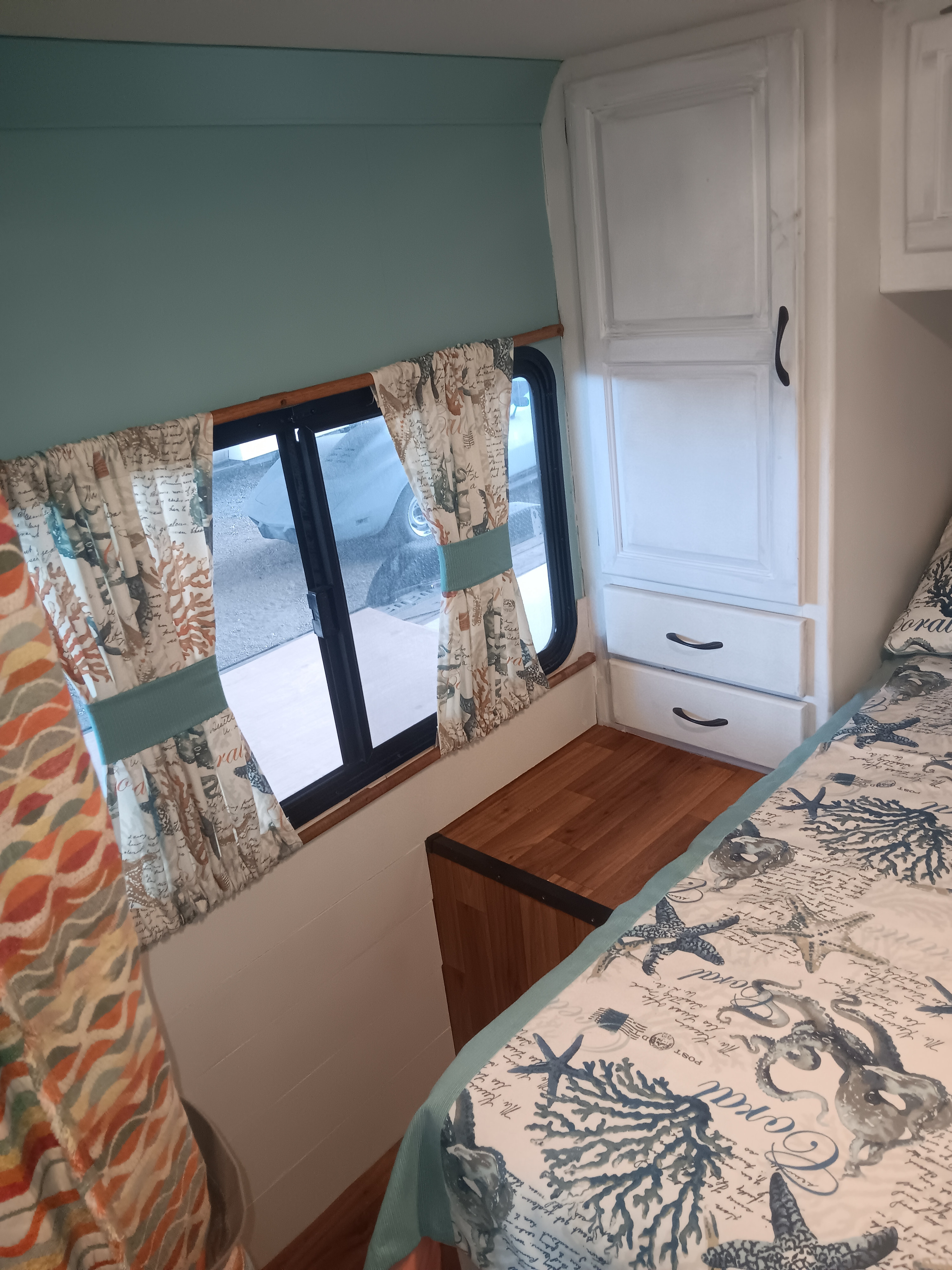 Cozy RV rental bedroom with coastal decor, including sea-themed curtains and comforter, and built-in storage.. Thor Majestic 2015
