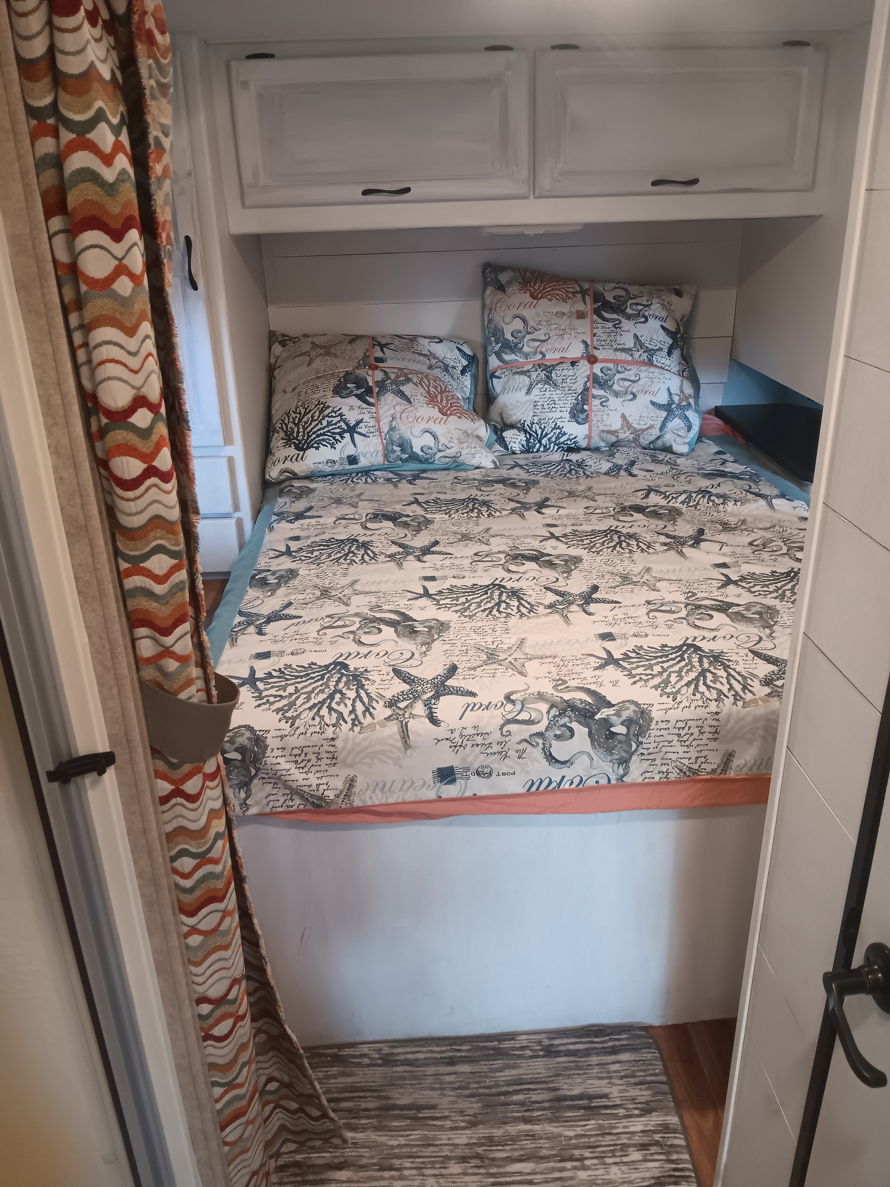 This RV rental bedroom features a bed with coastal marine decor, matching pillows, and white overhead cabinets.. Thor Majestic 2015