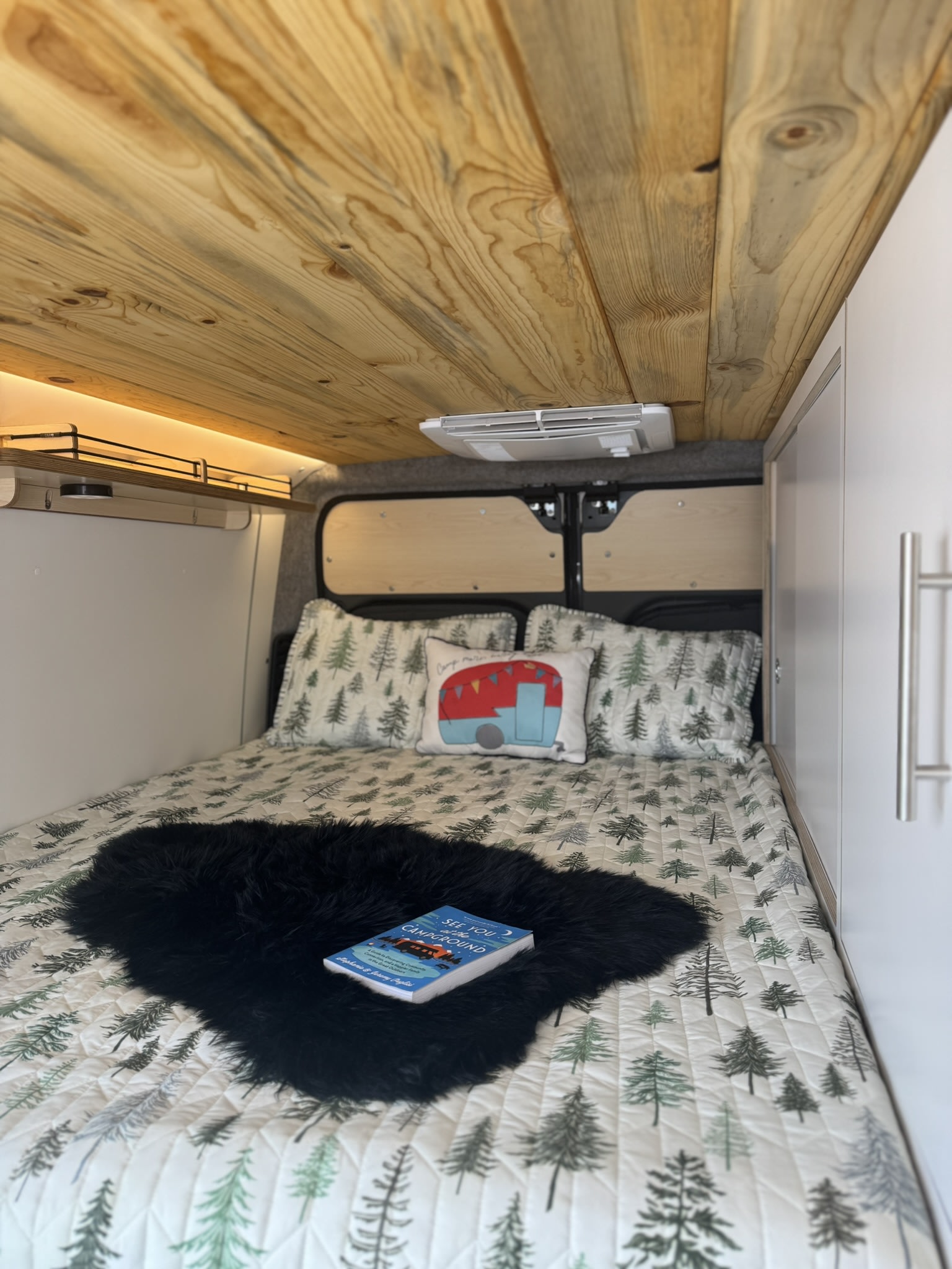 Cozy RV rental interior showcasing a bed with tree-patterned bedding, a camper pillow, and wooden ceiling.. DM Vans LV 7.1 2023