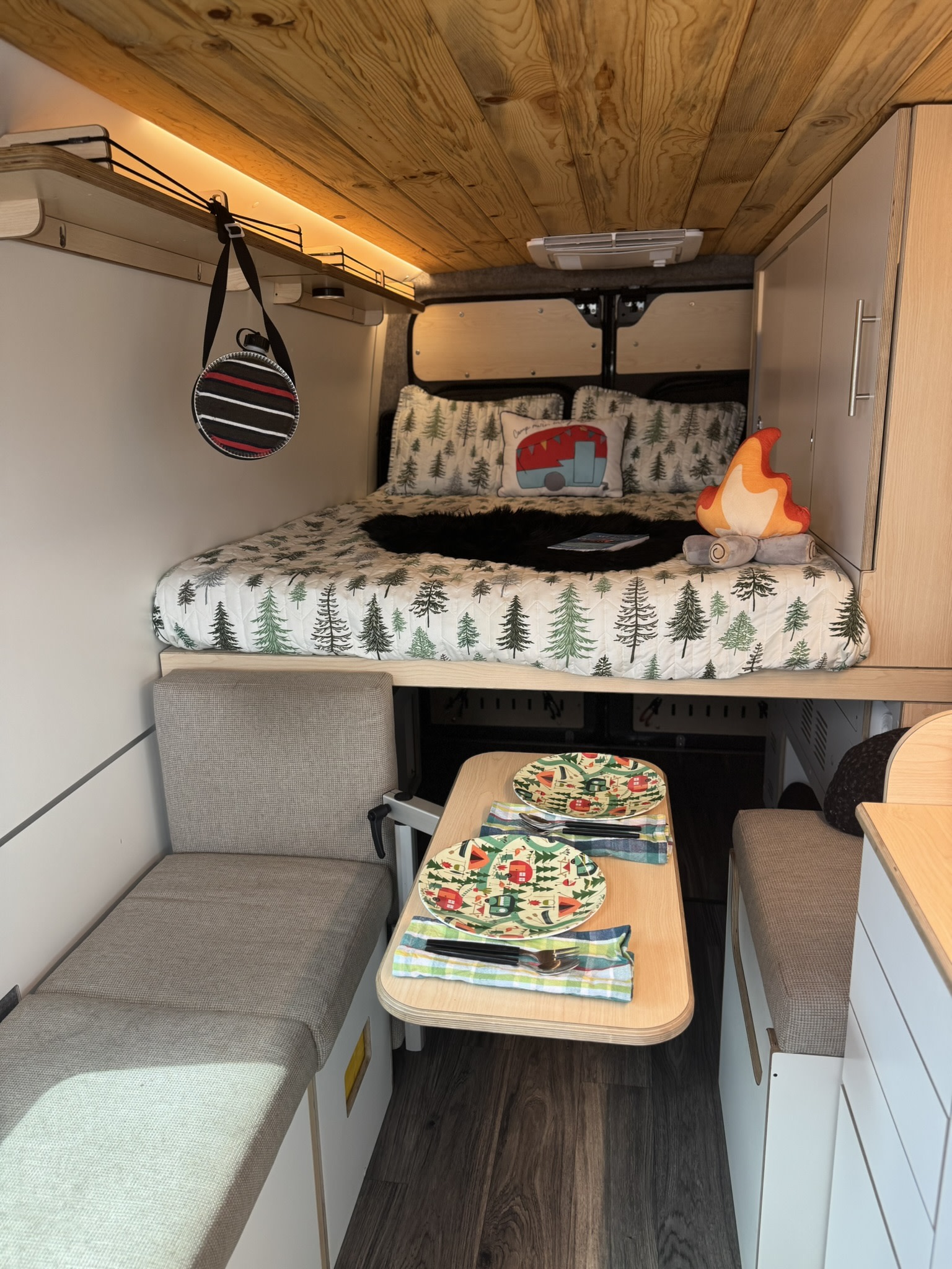 RV rental: a cozy bed with forest quilt rests above a charming dining area, set for two.. DM Vans LV 7.1 2023