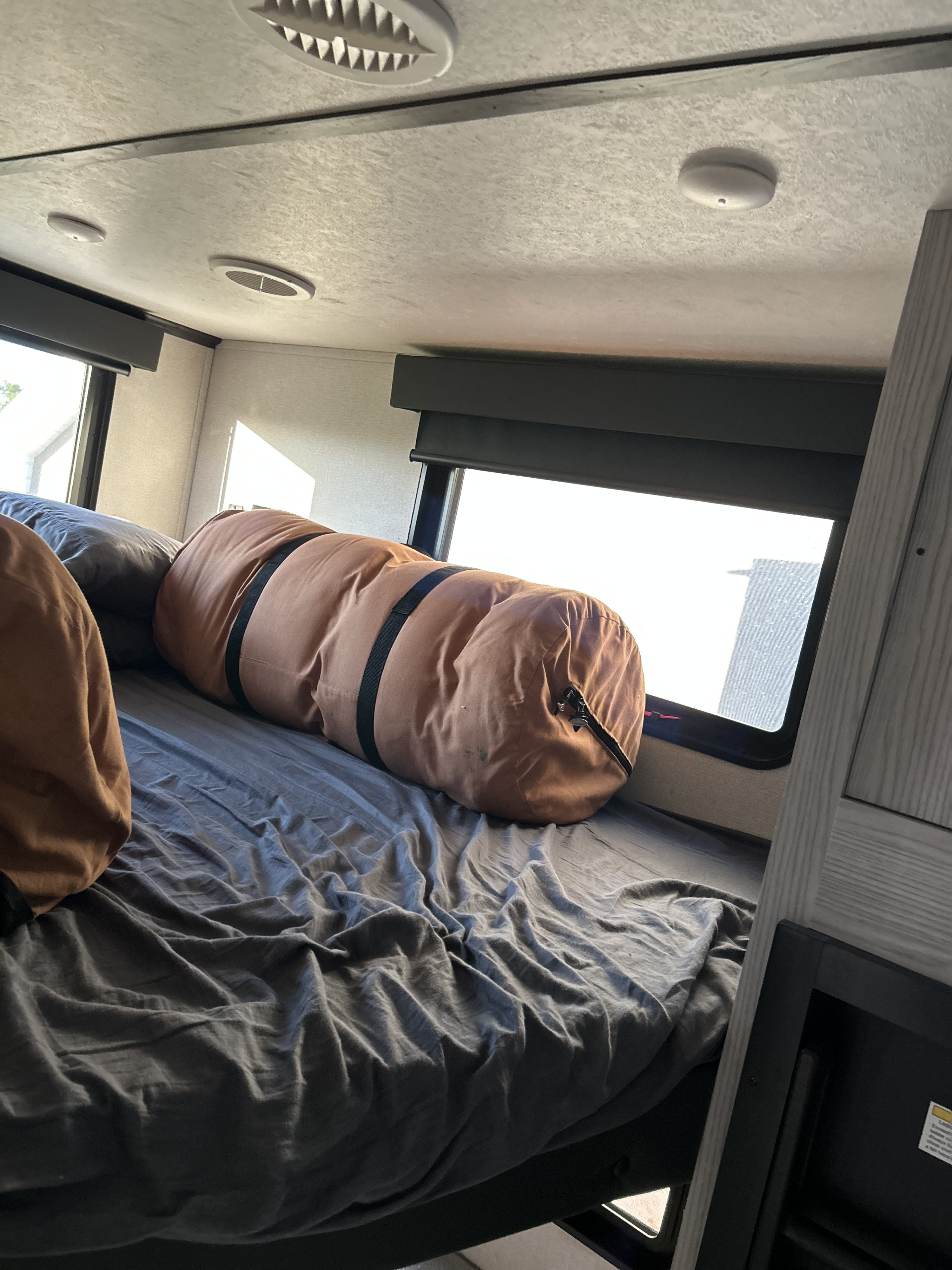 Comfortable RV rental bunk bed with pillows, gray sheets, and bright windows, showing a cozy interior space.. Keystone RV Montana High Country 2021
