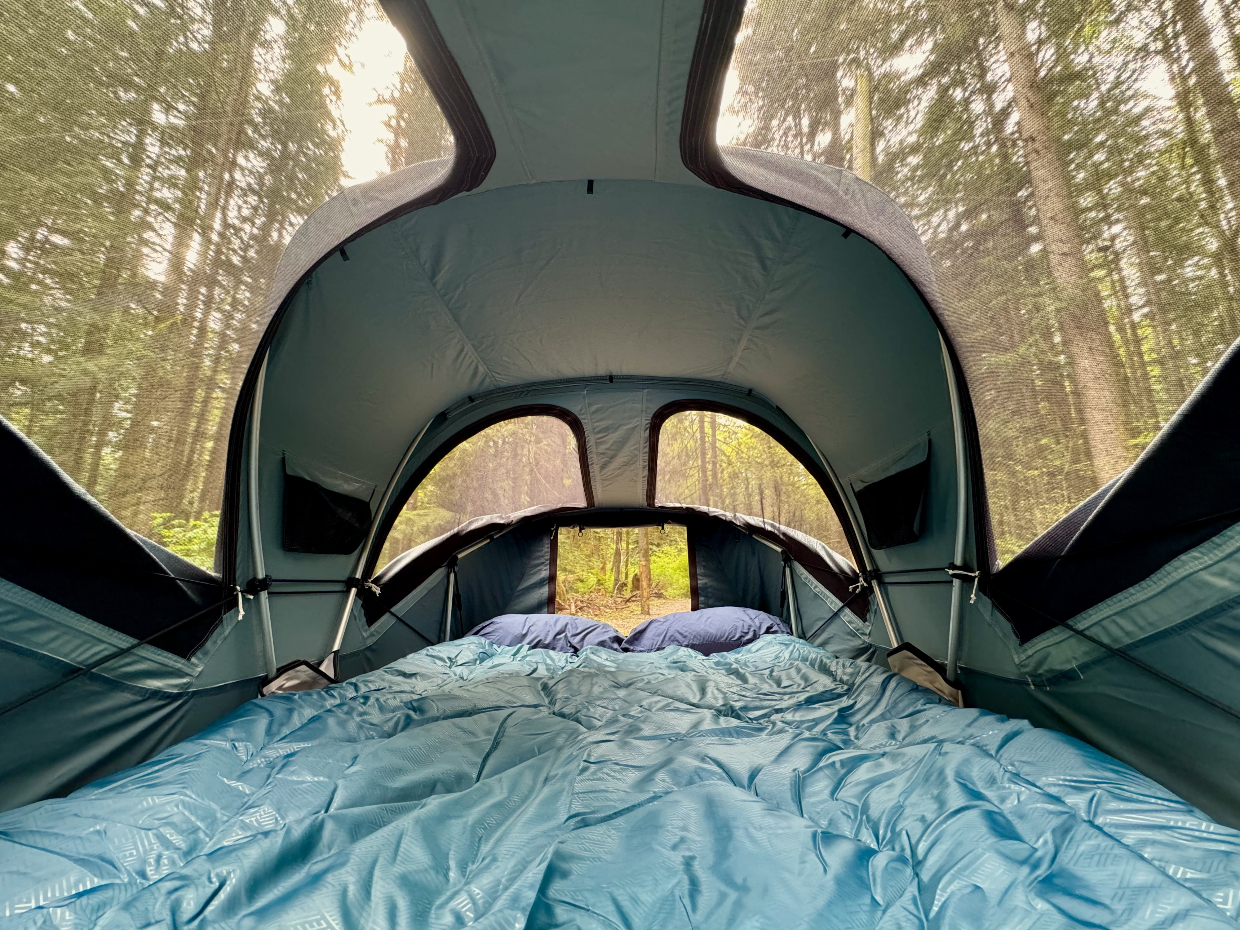 Inside a cozy rooftop tent from an rv rental, featuring a bed and stunning forest views. Ideal for nature lovers.. Ford Maverick 2025
