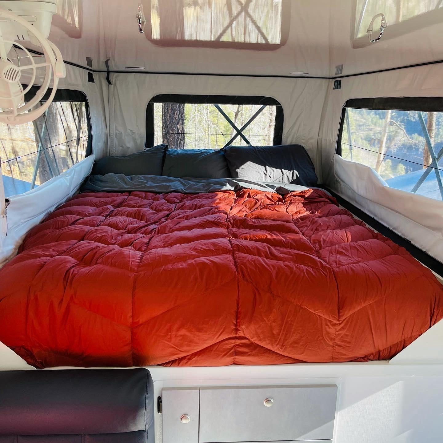 Cozy RV rental bedroom with a large bed, orange comforter, and forest views for your next camping adventure.. Lifestyle Campers Reconn R2 Elite 2021