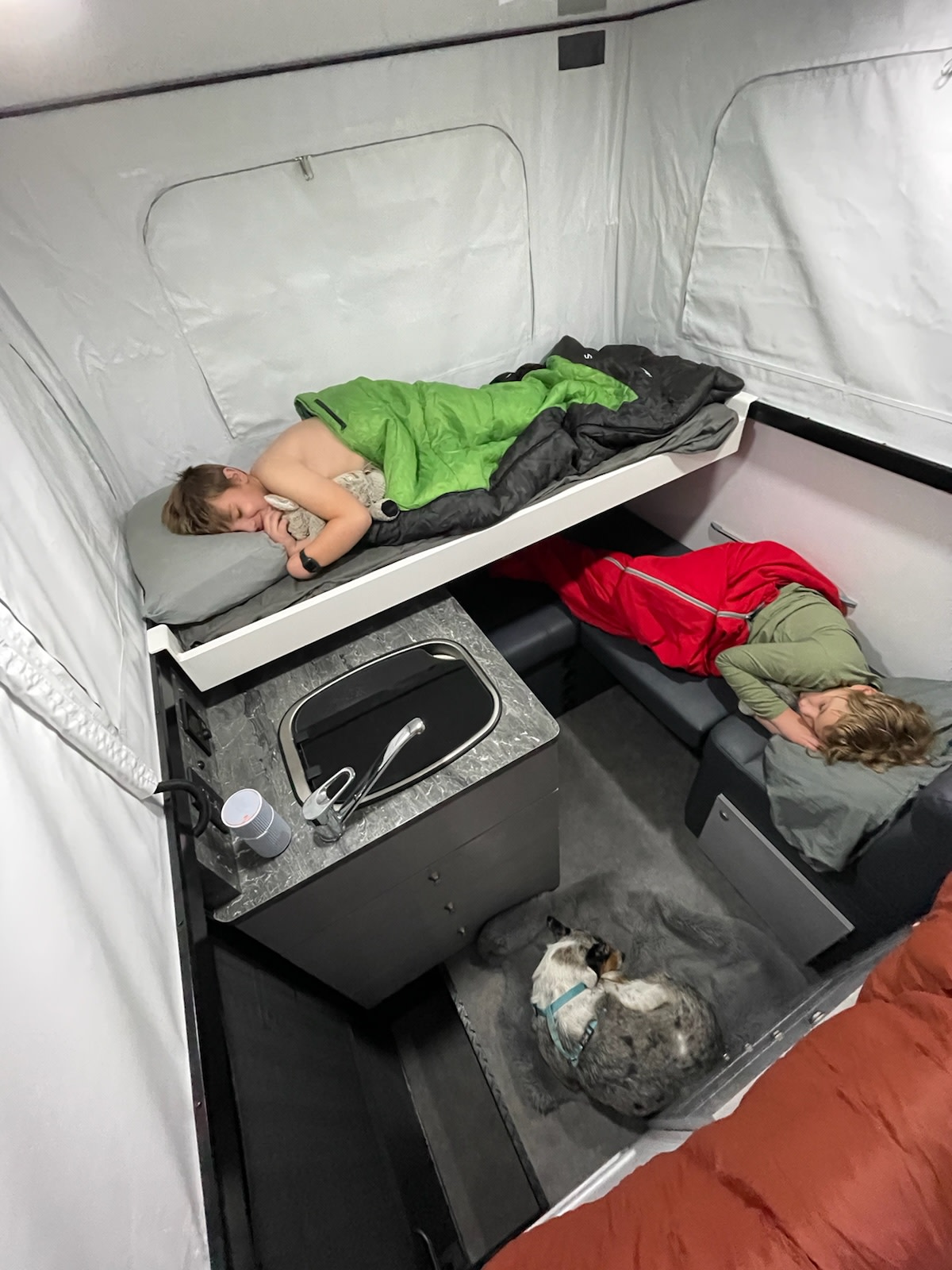 Two children nap on bunks, and a dog sleeps on the floor in a compact, well-equipped rv rental with a sink.. Lifestyle Campers Reconn R2 Elite 2021