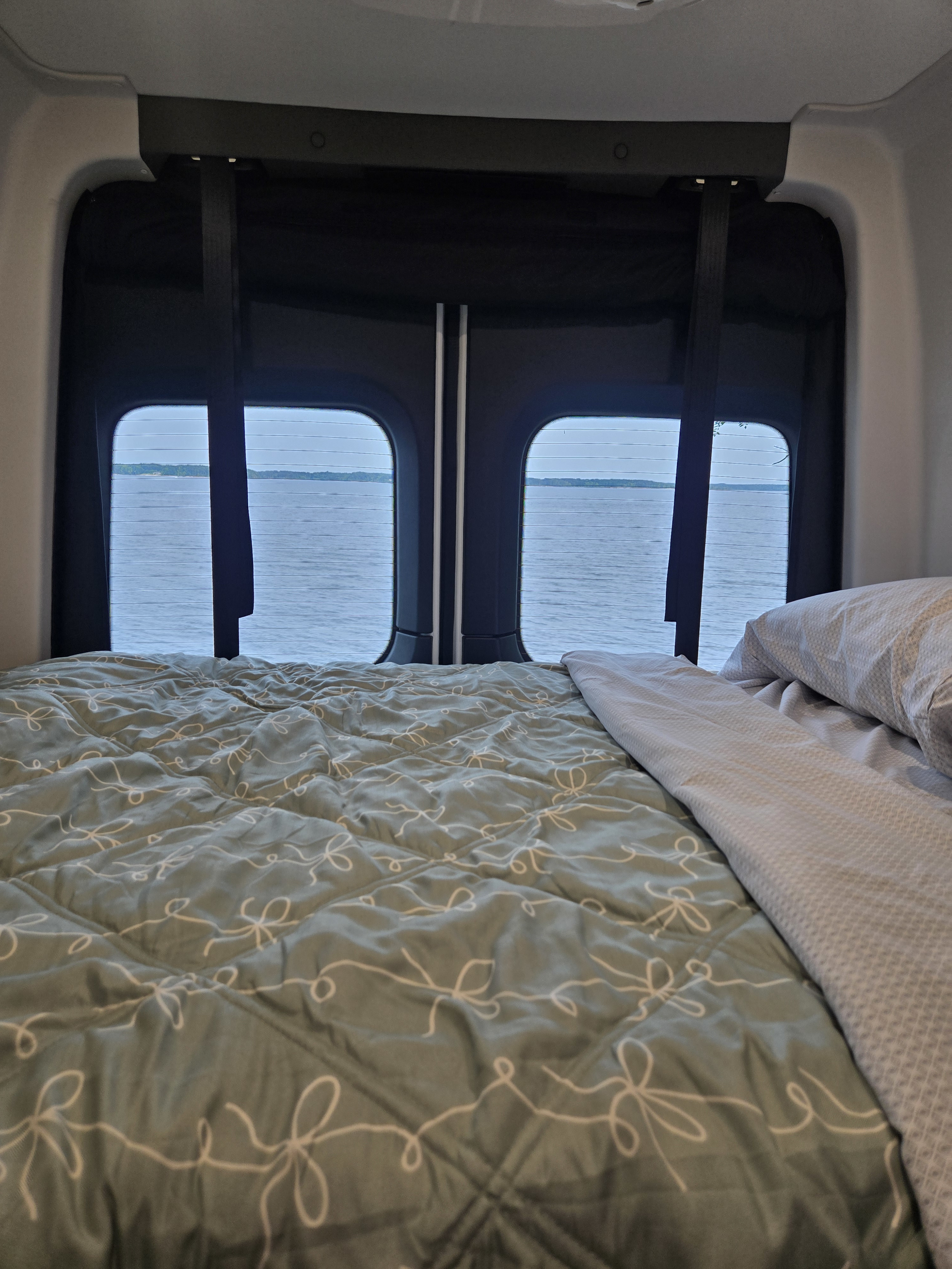 Peaceful rv rental interior: A cozy bed faces large windows with a scenic view of a calm lake.. GH1 GH1 Class B 2025