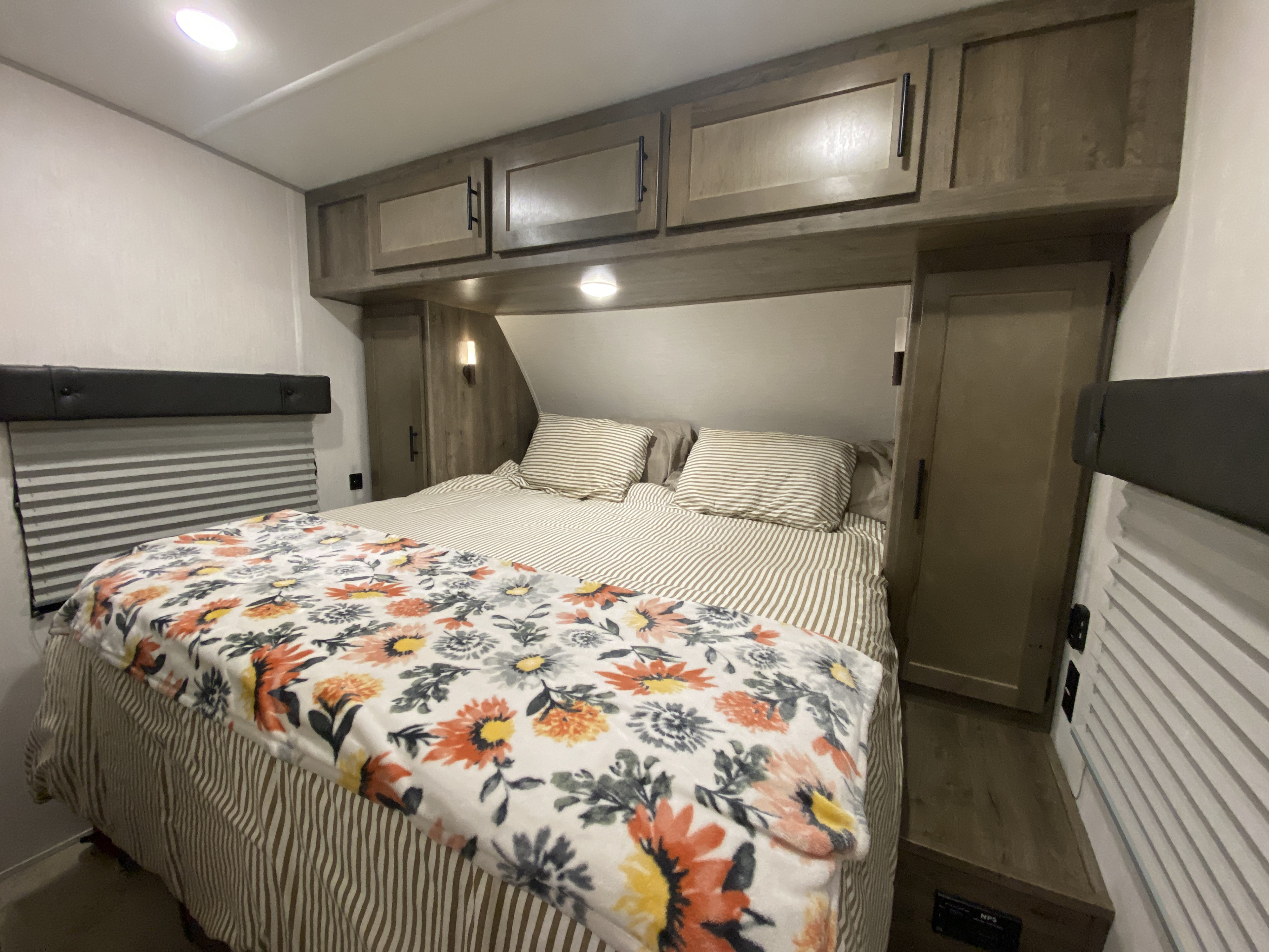 Cozy RV rental bedroom showcasing a bed with striped bedding, a floral blanket, overhead cabinets, and window blinds.. Forest River Vengeance 2021