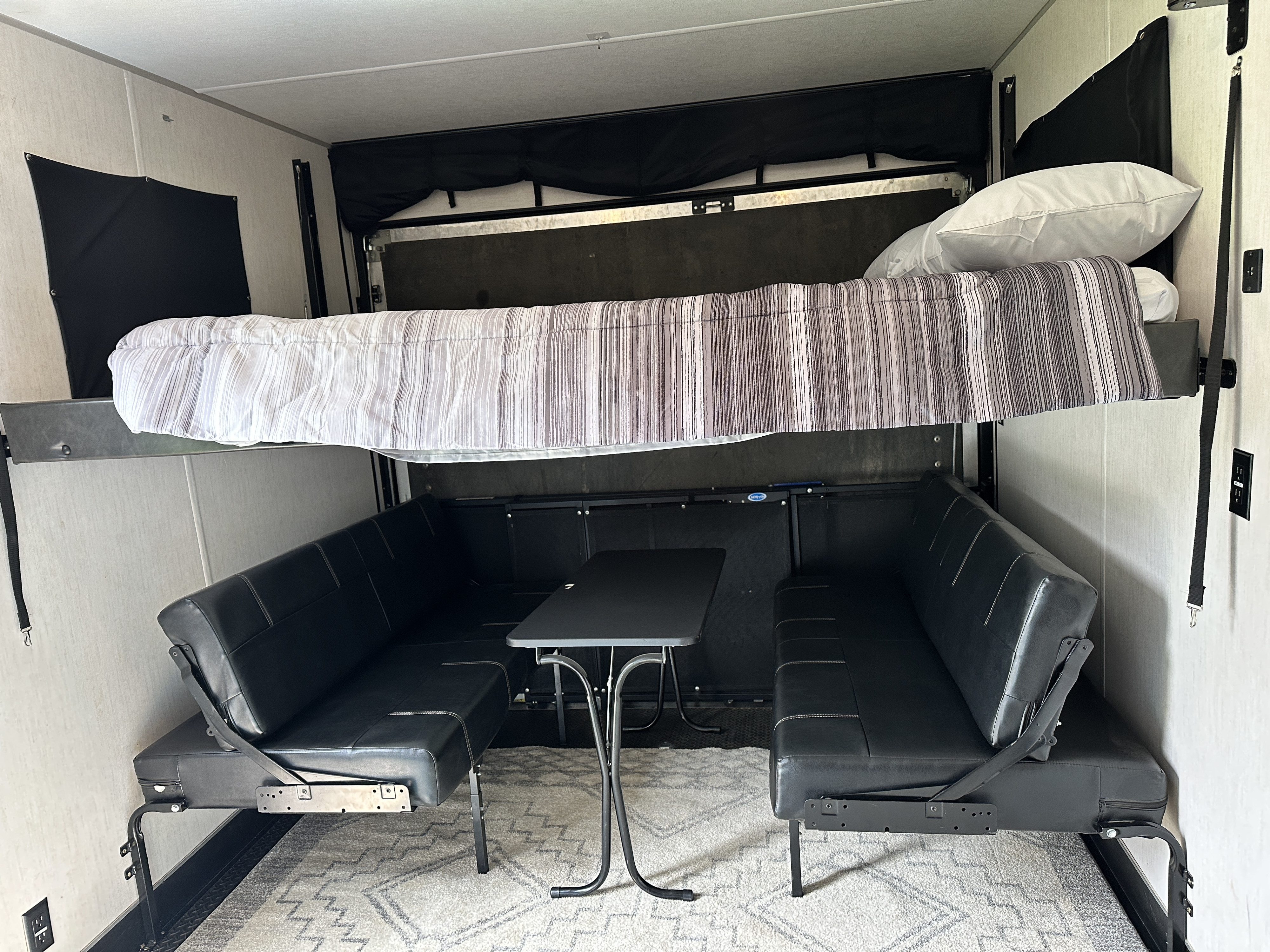 This RV rental interior features convertible bunk beds, two black couches, and a table, maximizing compact living space.. Forest River Vengeance 2021