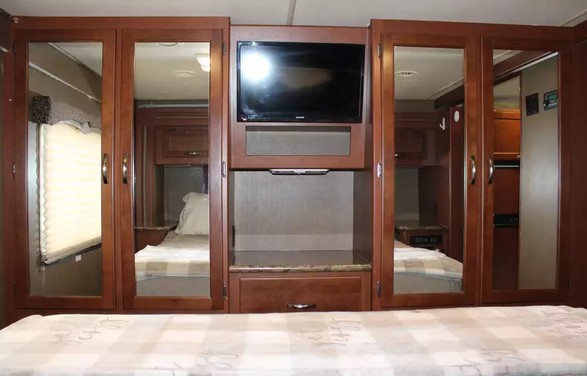 RV rental interior: bedroom features a mounted TV, mirrored wardrobes, and a comfy bed with checkered linens.. Thor Four Winds 2015