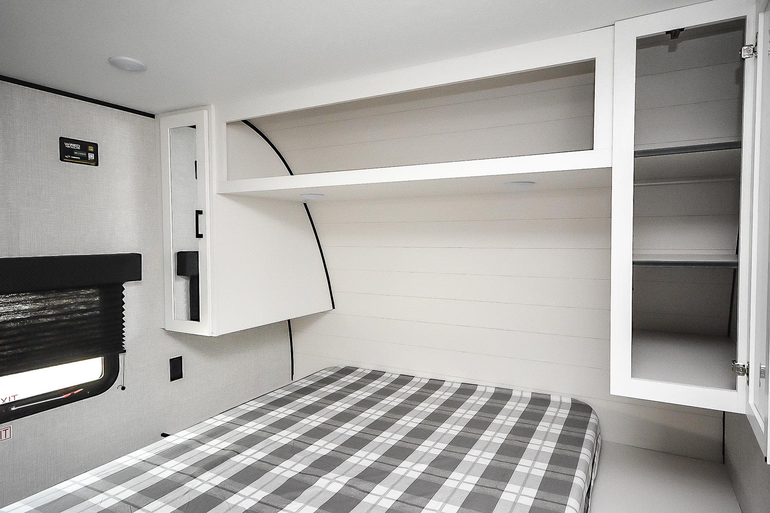 Inside an RV rental bedroom featuring a plaid bed, white overhead storage, and wall paneling. Includes window.. Jayco Jay Flight 260BH 2025
