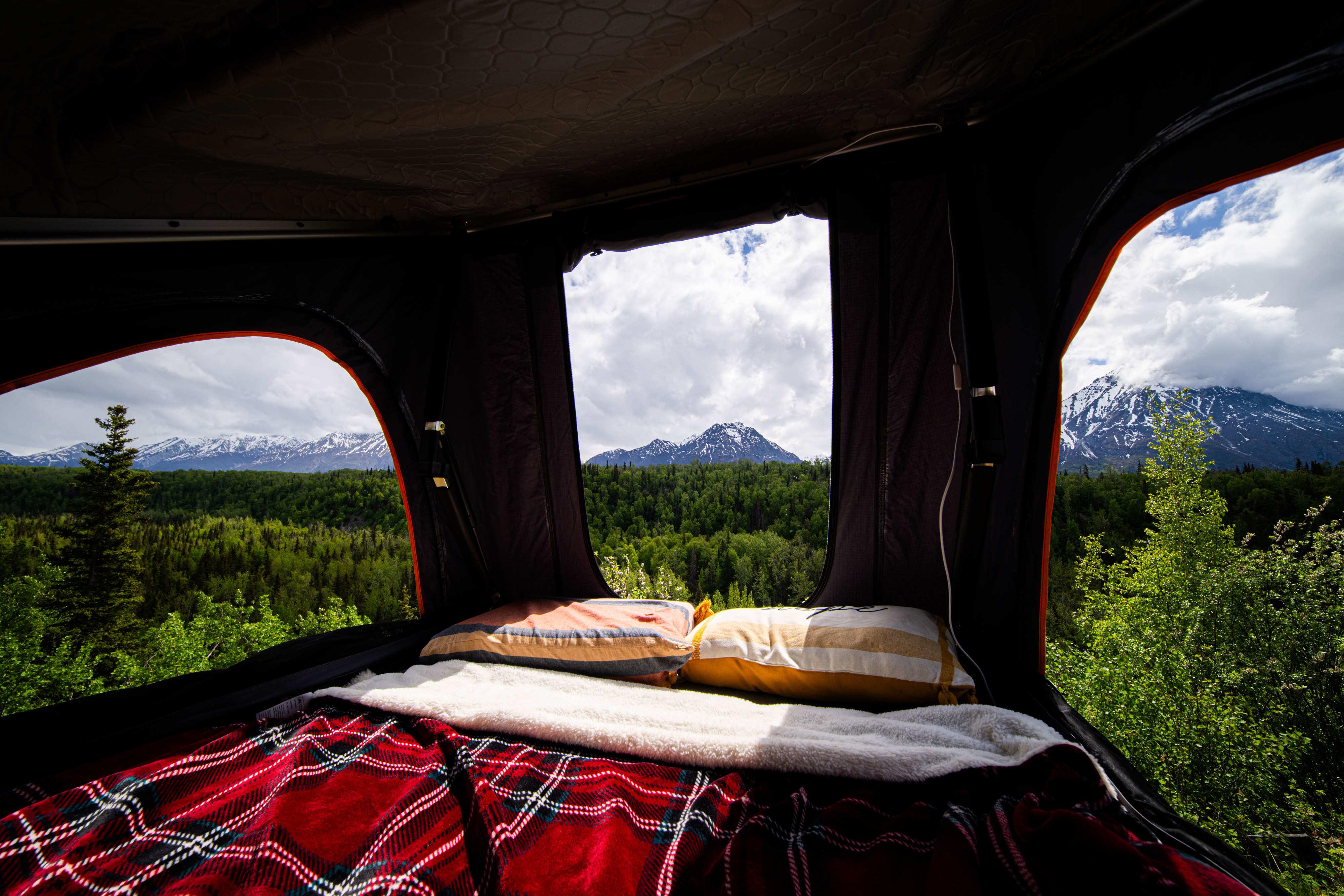 Cozy interior of an RV rental rooftop tent with a bed, offering stunning views of snow-capped mountains and green forests.. Honda Element 2008