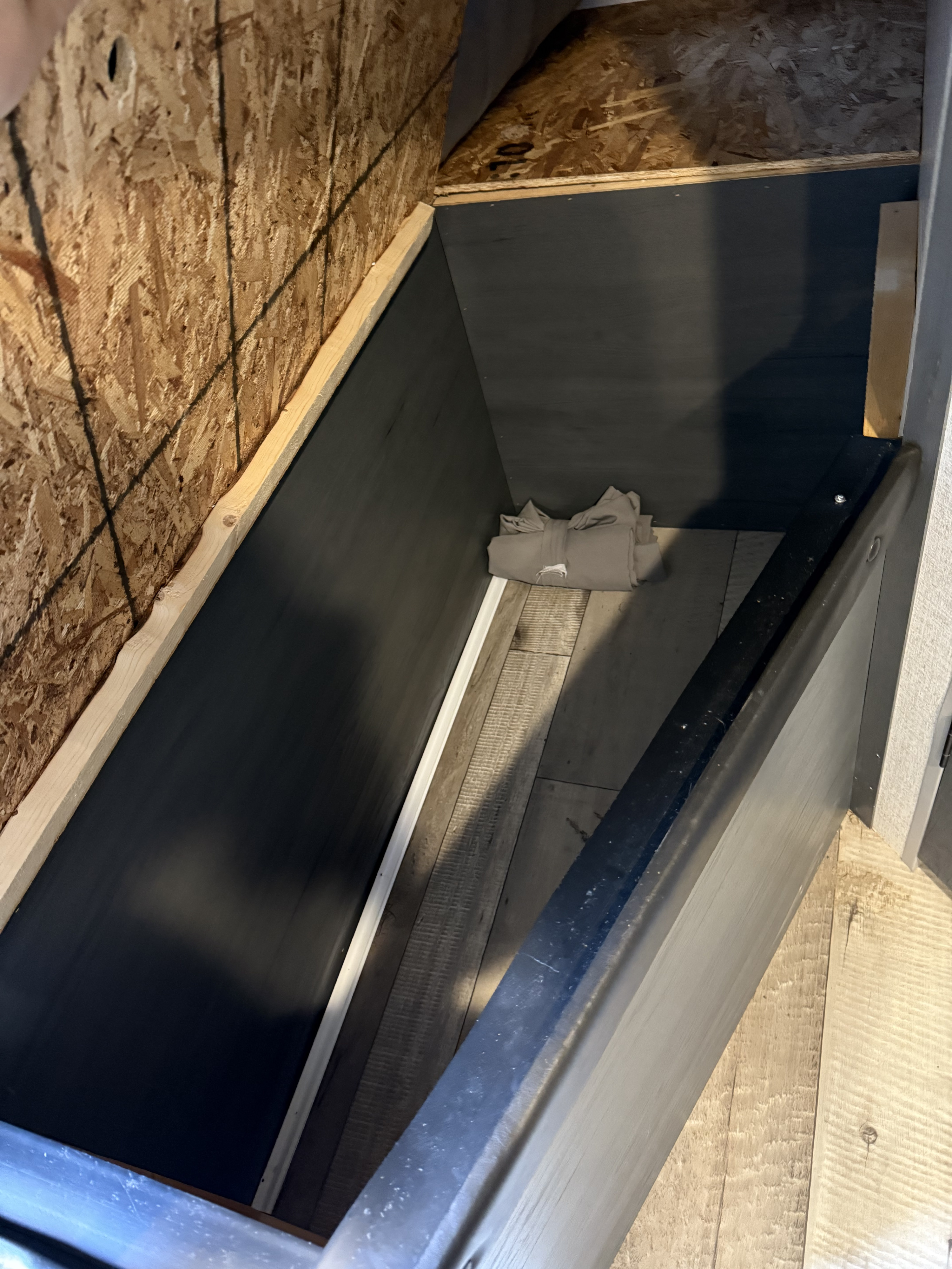 This RV rental's interior storage compartment has dark paneling, wood-look flooring, and an OSB wall; a neatly folded item sits inside.. Aspen Trail Aspen Trail Trailer 2022