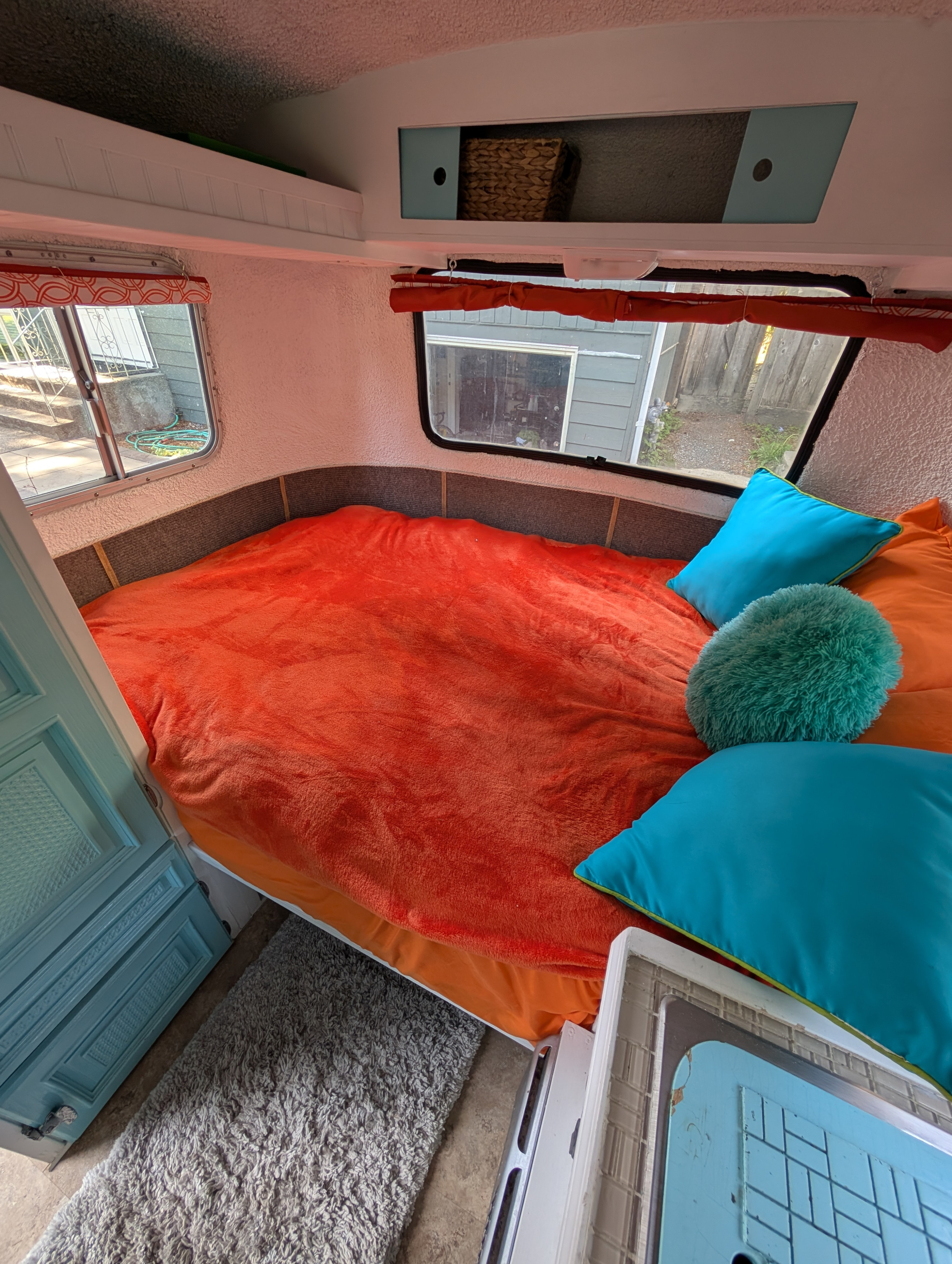 Inside an RV rental: A cozy bedroom with a large orange bed, teal pillows, and functional overhead storage.. Boler Neonex 1300 1979