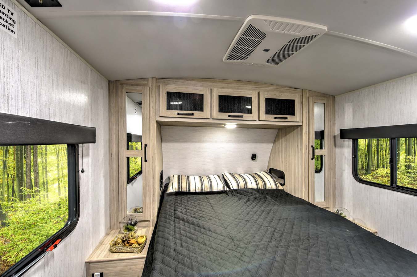Comfortable RV rental bedroom with bed, overhead cabinets, and large windows showing a vibrant forest.. Heartland RVs Sundance Ultra Lite 2022