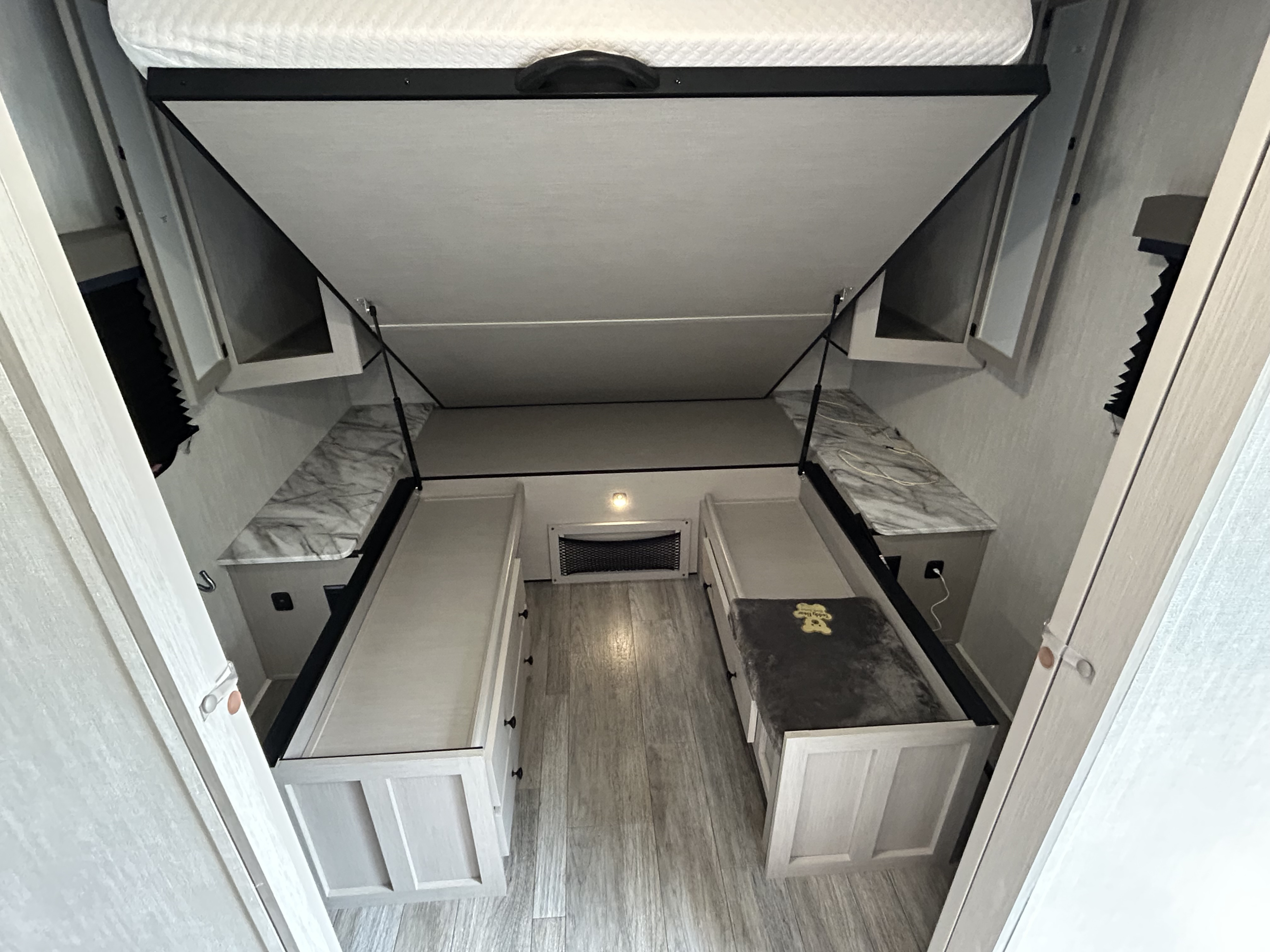 RV rental interior: a lifted main bed reveals two lower storage benches/daybeds, maximizing usable living space.. Forrest River Apex Ultra Lite 291TBSS 2025