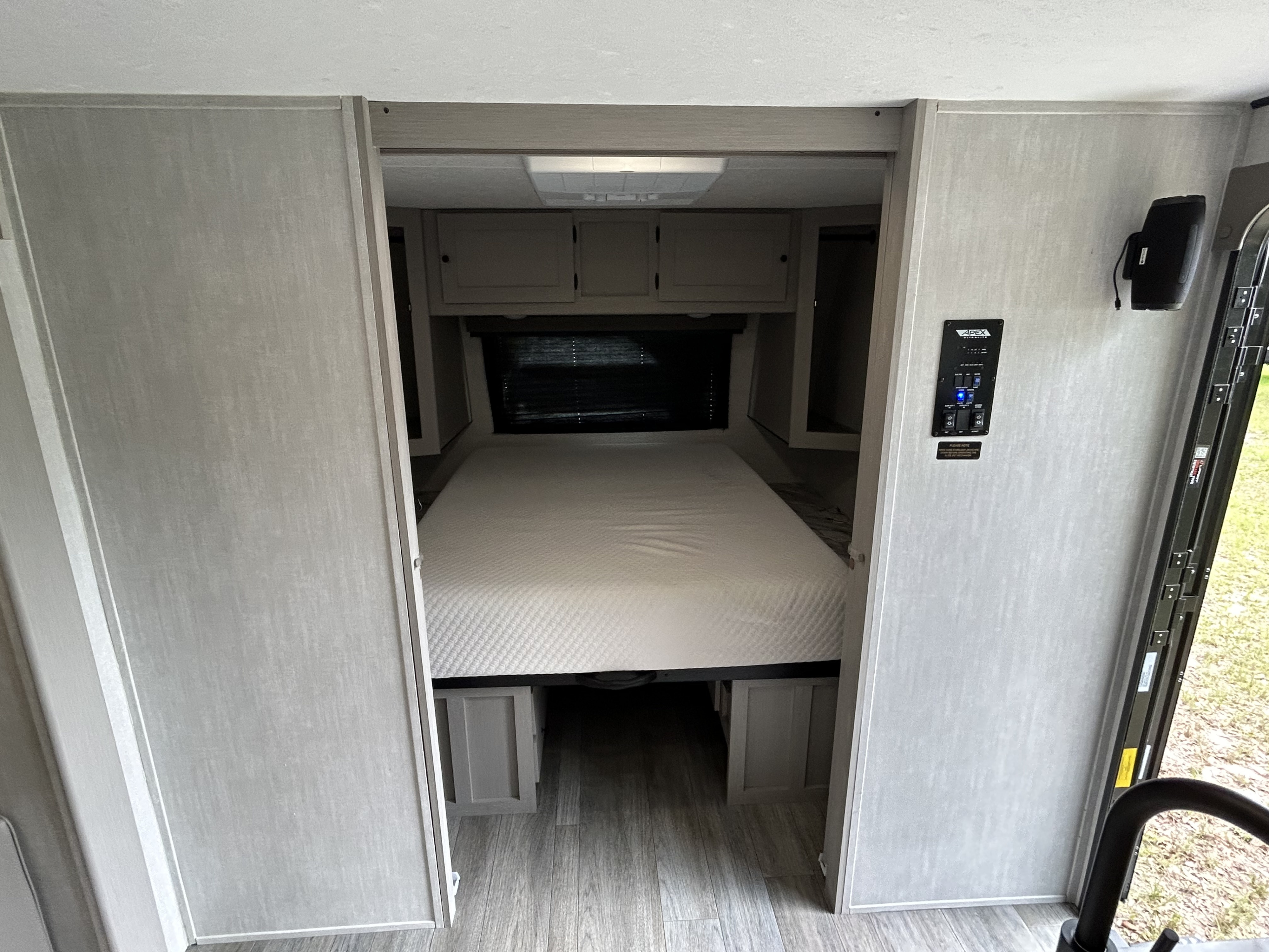 This RV rental interior features a cozy bedroom with a comfortable bed, overhead storage, and control panel access.. Forrest River Apex Ultra Lite 291TBSS 2025