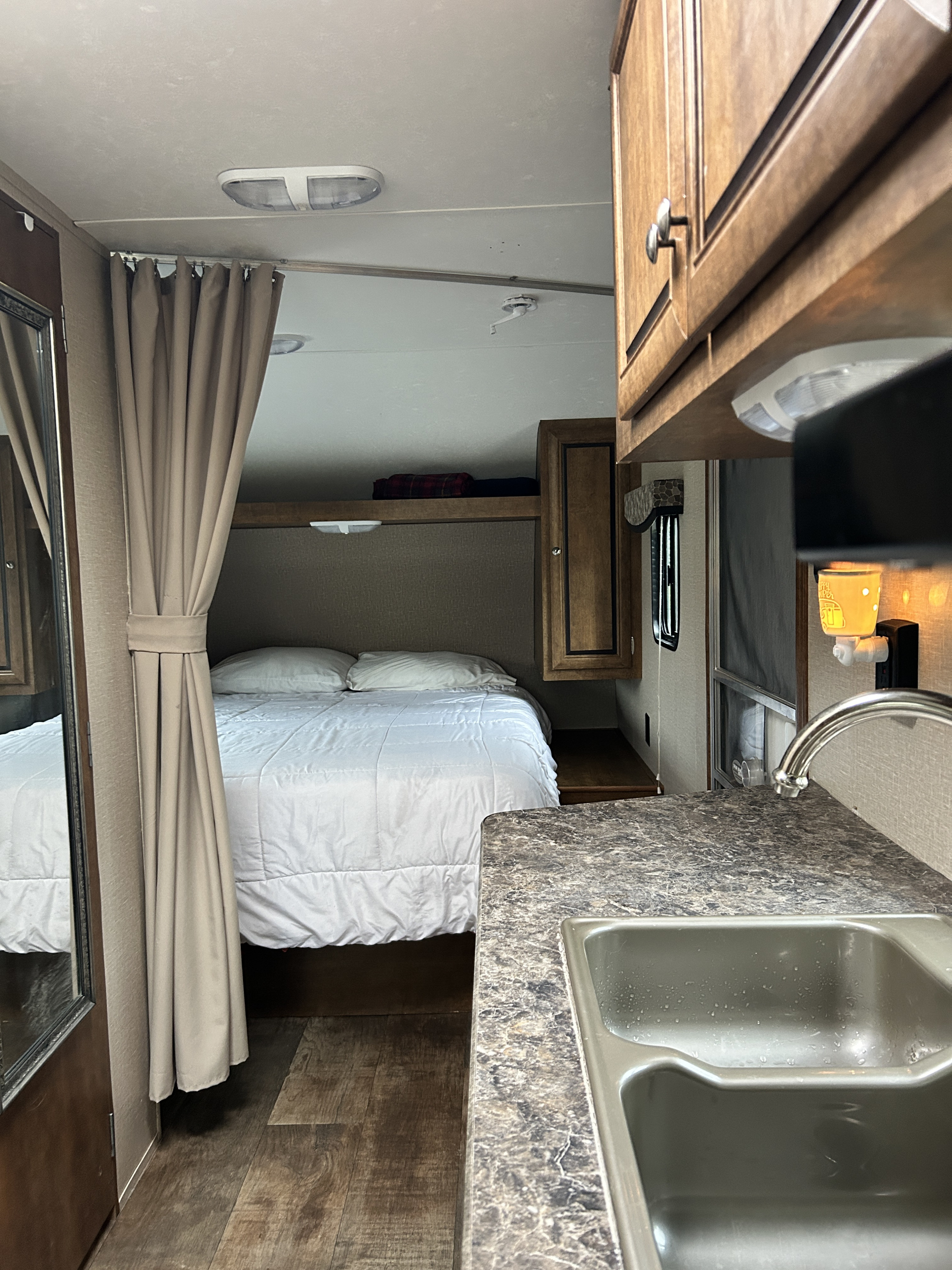 Cozy RV rental interior showing a bedroom with a white bed, privacy curtain, and a compact kitchen counter with sink.. Crossroads Z-1 2017
