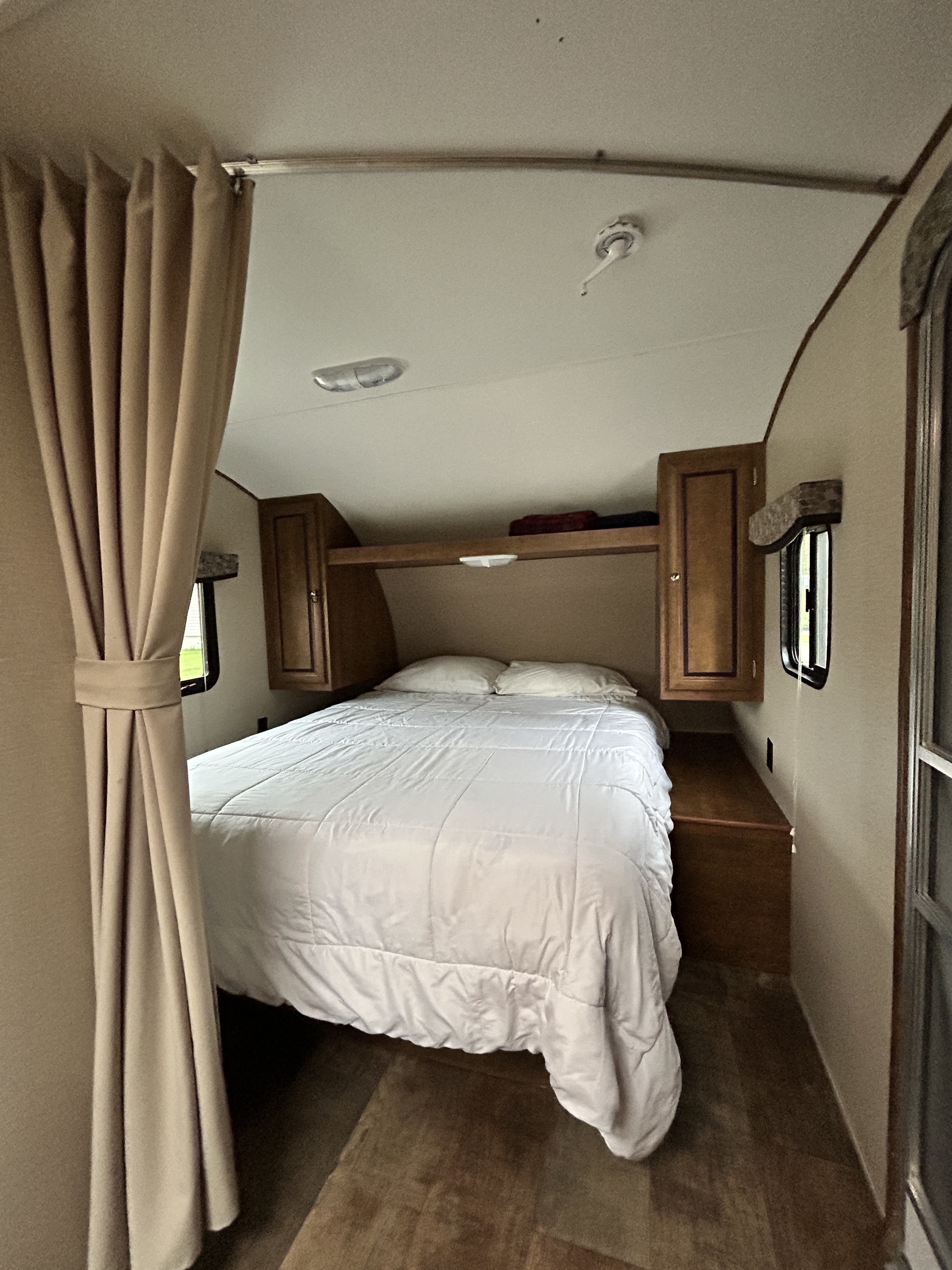 Compact RV rental bedroom featuring a neat bed, overhead cabinets, and light curtains for privacy.. Crossroads Z-1 2017