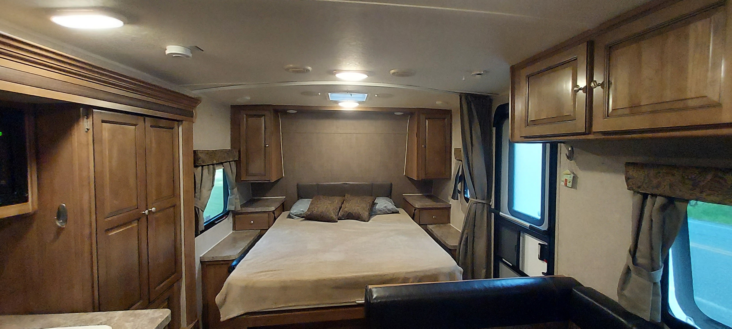 Comfortable RV rental bedroom featuring a queen-sized bed, overhead cabinets, and large windows, ideal for travel.. Forest River Rockwood Mini Lite 2016