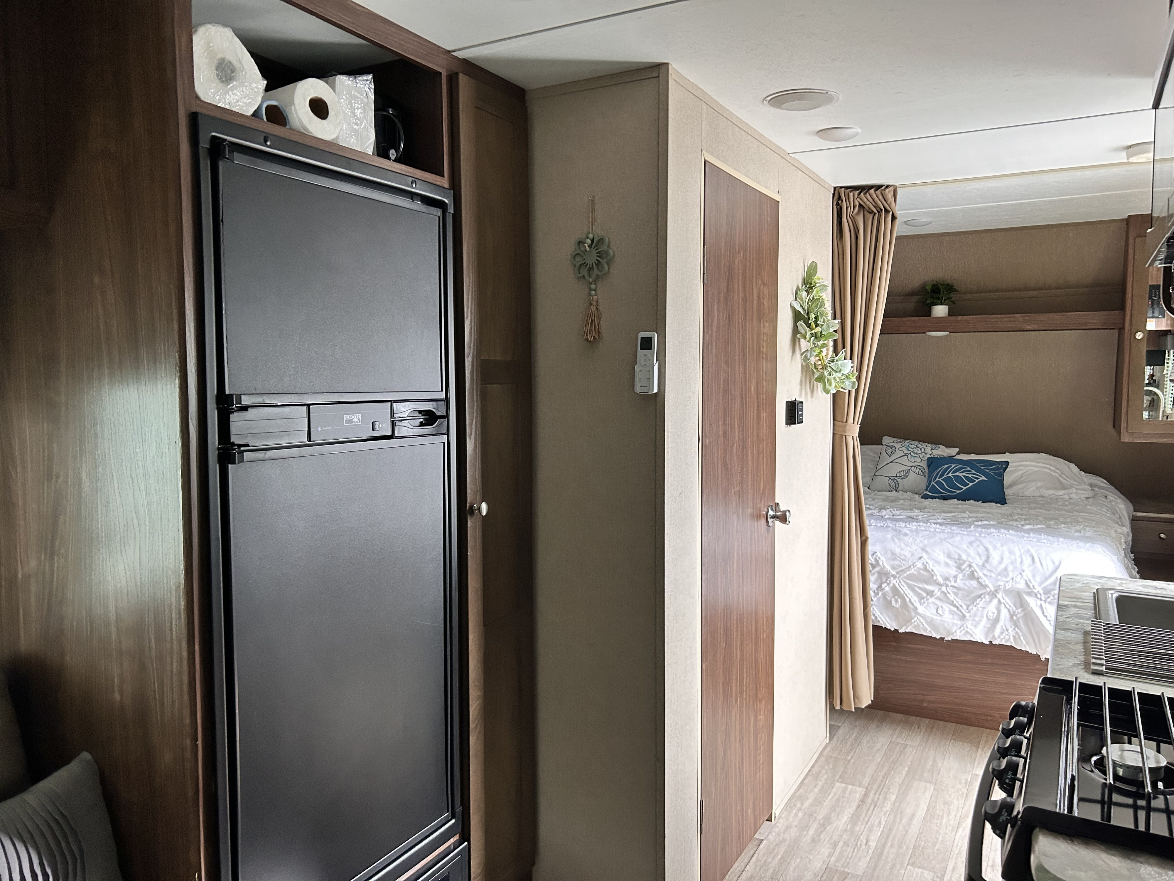 RV rental interior: A compact living space featuring a fridge, cozy bedroom with white bedding, and kitchen.. Dutchmen Coleman Lantern 2018