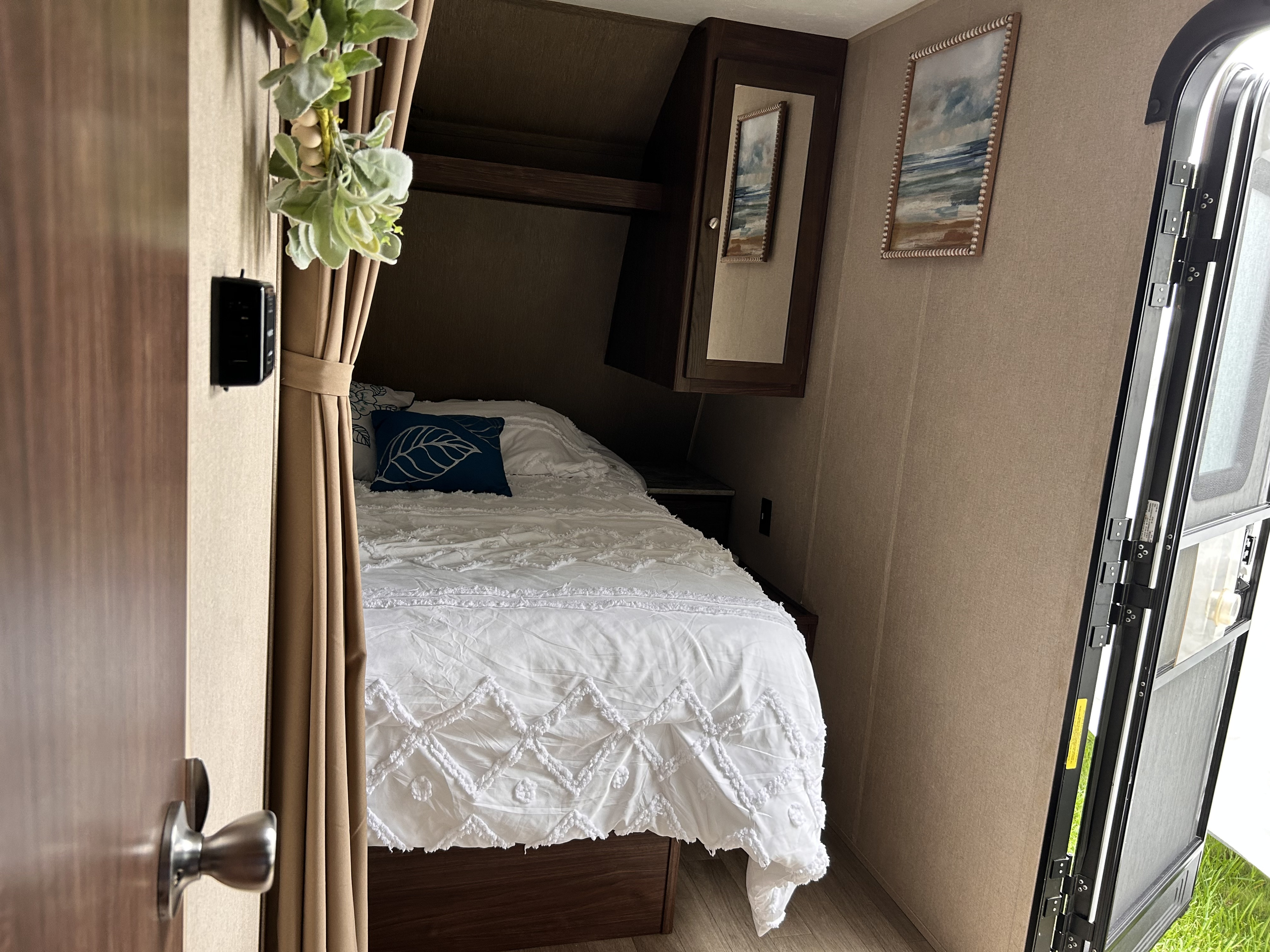 Cozy RV rental bedroom featuring clean white bedding, overhead storage, and homey decor for comfortable travels.. Dutchmen Coleman Lantern 2018