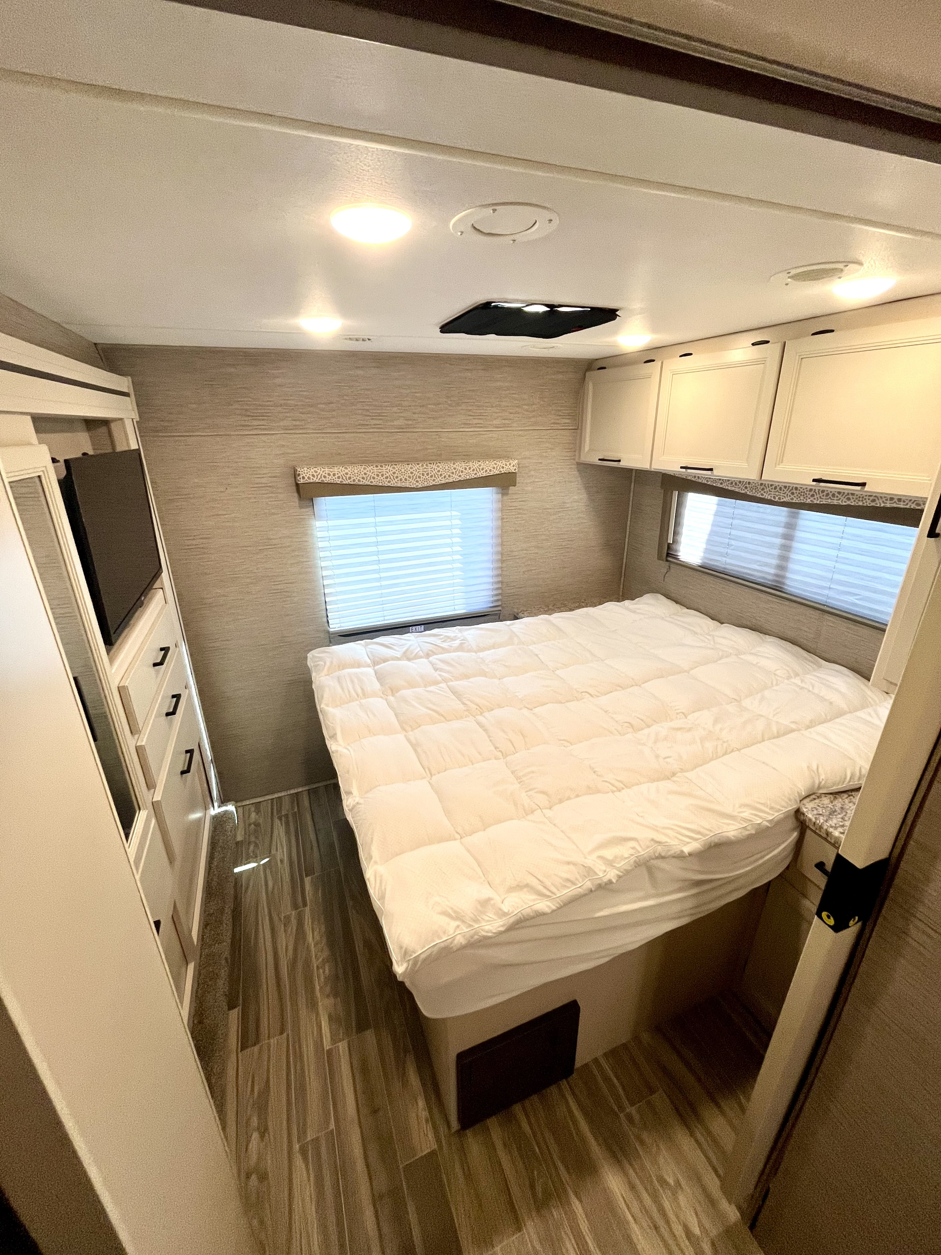 Cozy RV rental bedroom featuring a comfy white bed, overhead cabinets, window with blinds, and TV dresser.. Thor Freedom Elite 2022