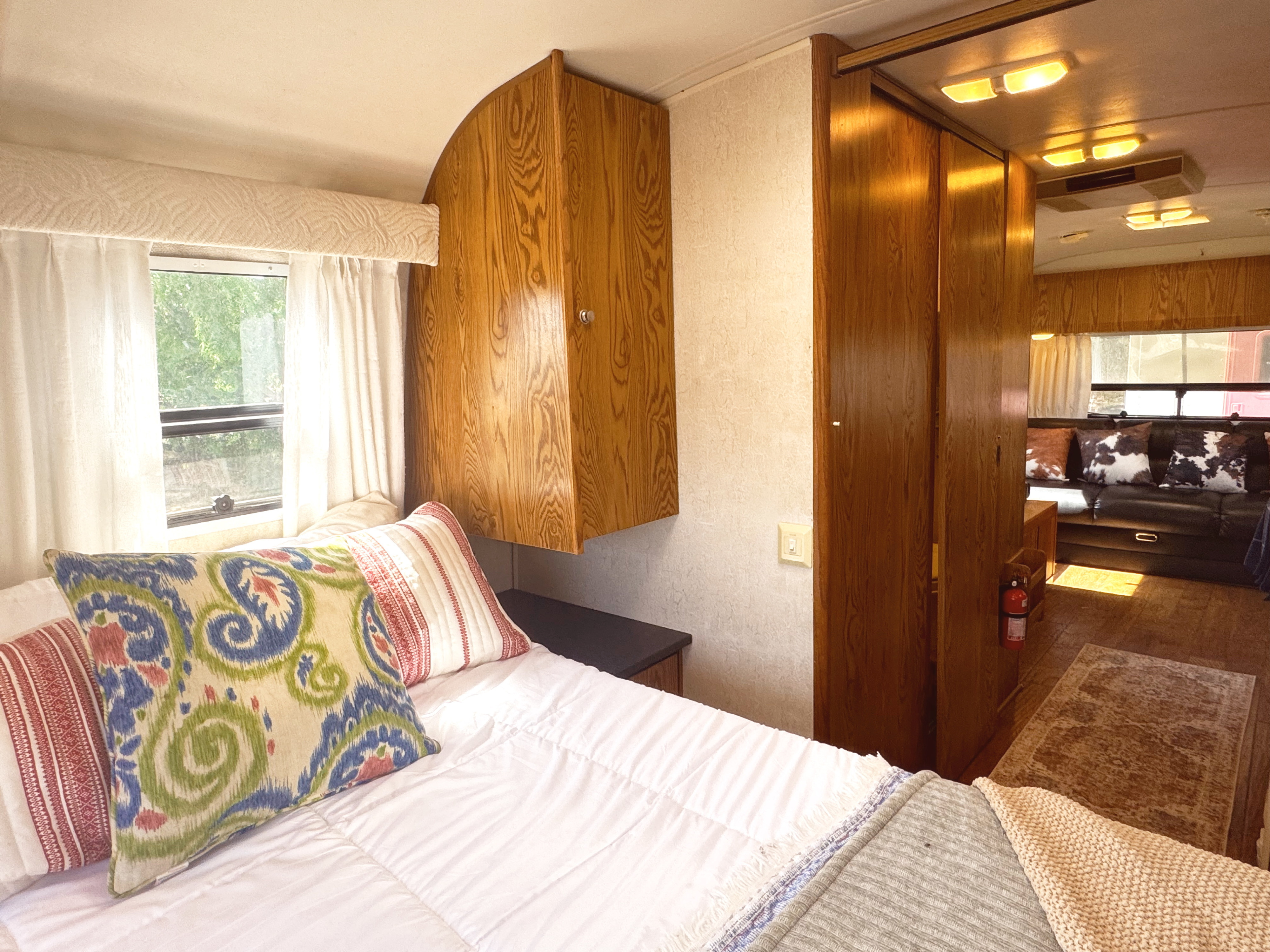 Cozy RV rental interior: a bedroom with pillows and window, looking into the living space with a couch.. Airstream Safari 2006