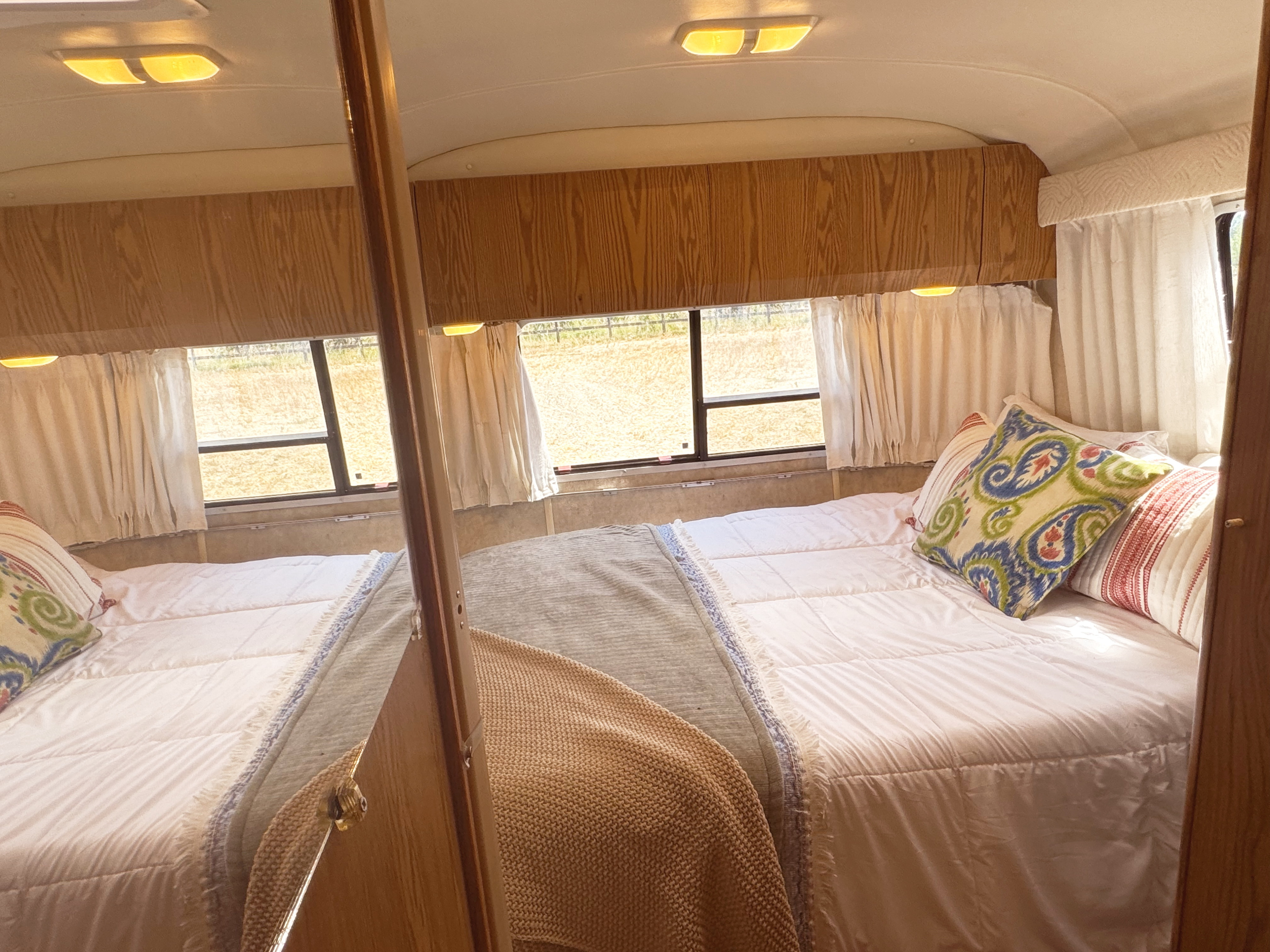 Bright RV rental bedroom: white bedding, colorful pillows, and wood cabinets, with scenic outdoor views.. Airstream Safari 2006