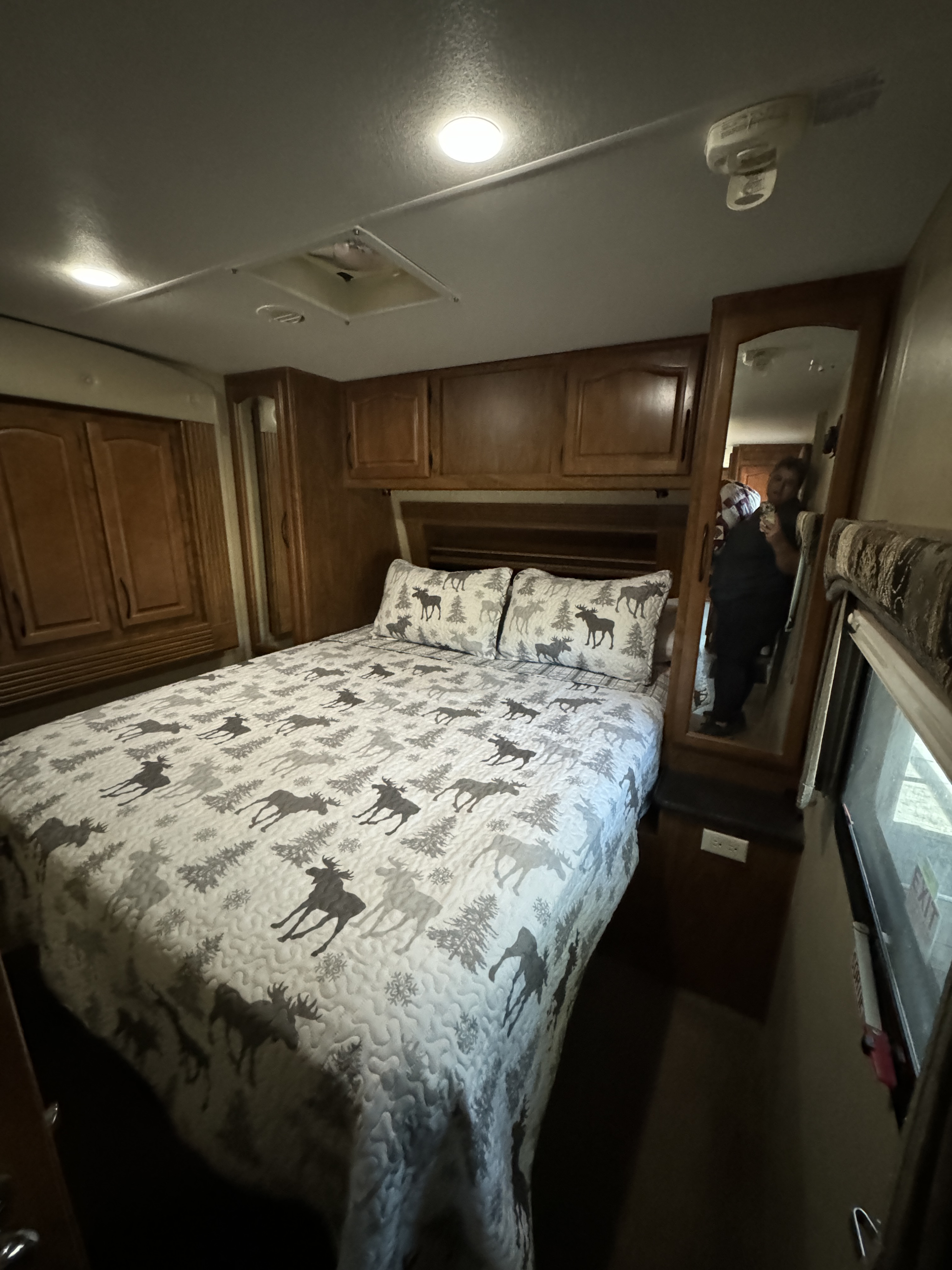Cozy RV rental bedroom with moose-patterned bedding, ample storage, and a full-length mirror. Perfect for travel comfort.. Outdoors RV Wind River 270RLDS 2013