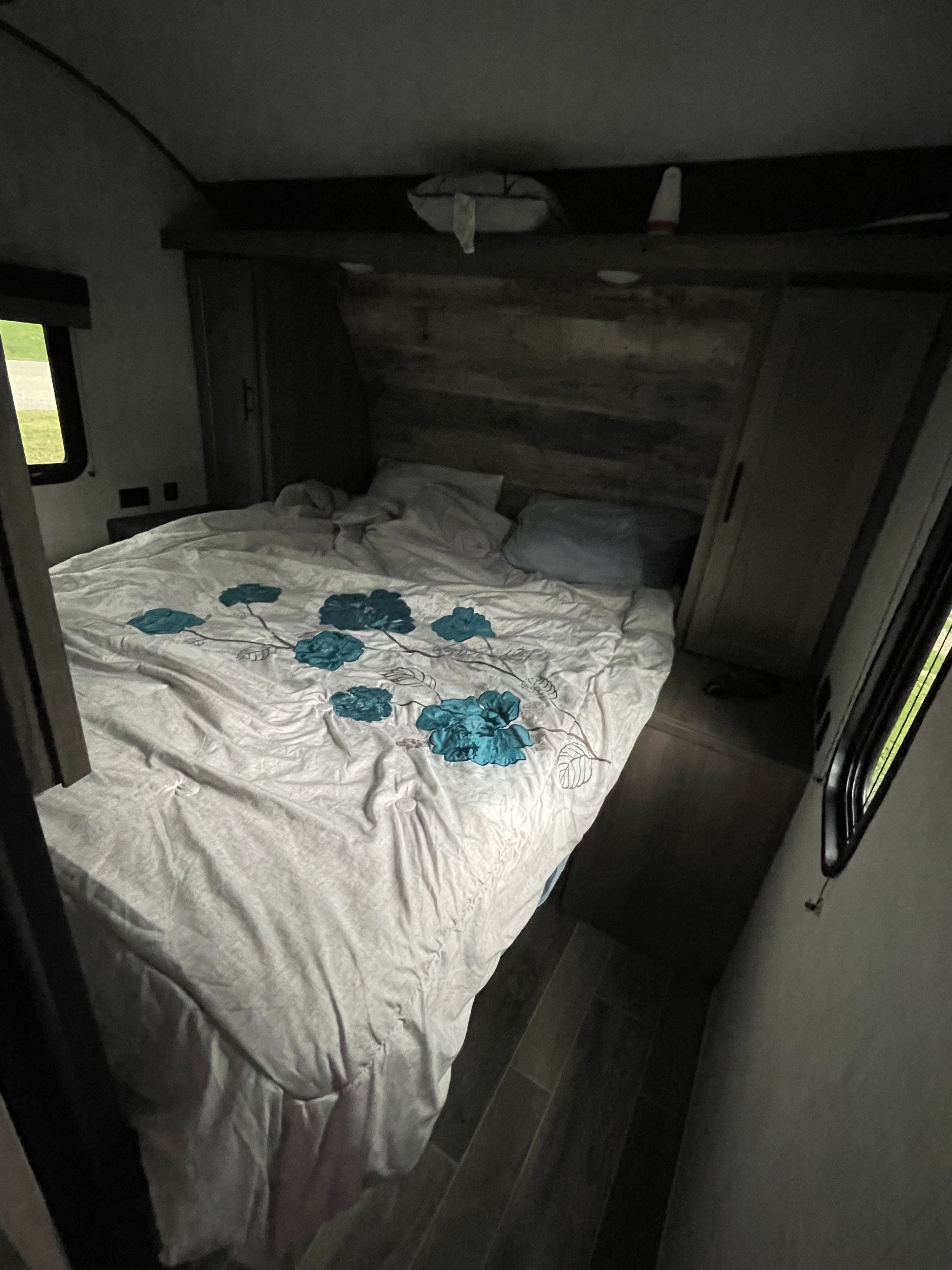 Relax in this cozy **RV rental** bedroom. Features a white bed with blue floral comforter, overhead storage, and window views.. Gulf Stream Ameri-Lite 2022