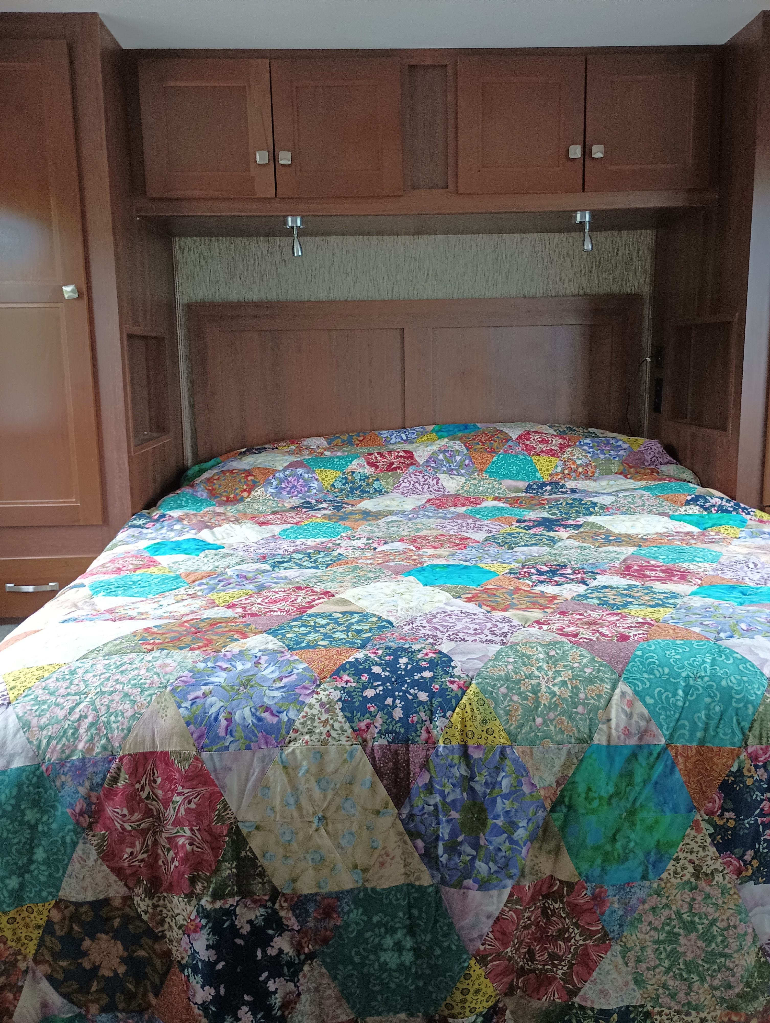 Vibrant patchwork quilt on a bed in an RV rental bedroom with overhead wood storage.. Forest River Sunseeker 2018