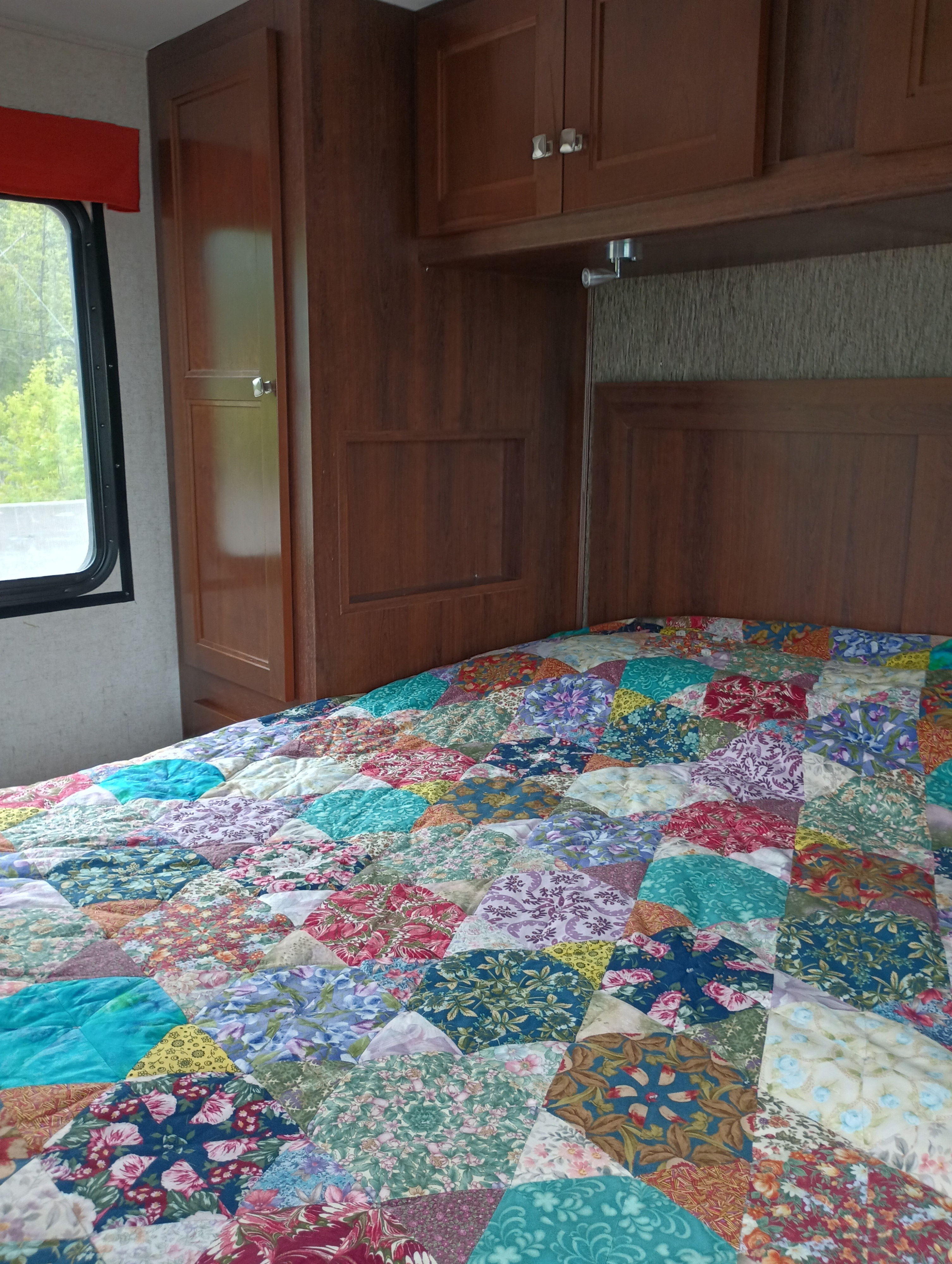 Cozy RV bedroom with a vibrant patchwork quilt, wooden cabinets, and window. Explore comfort in an rv rental.. Forest River Sunseeker 2018